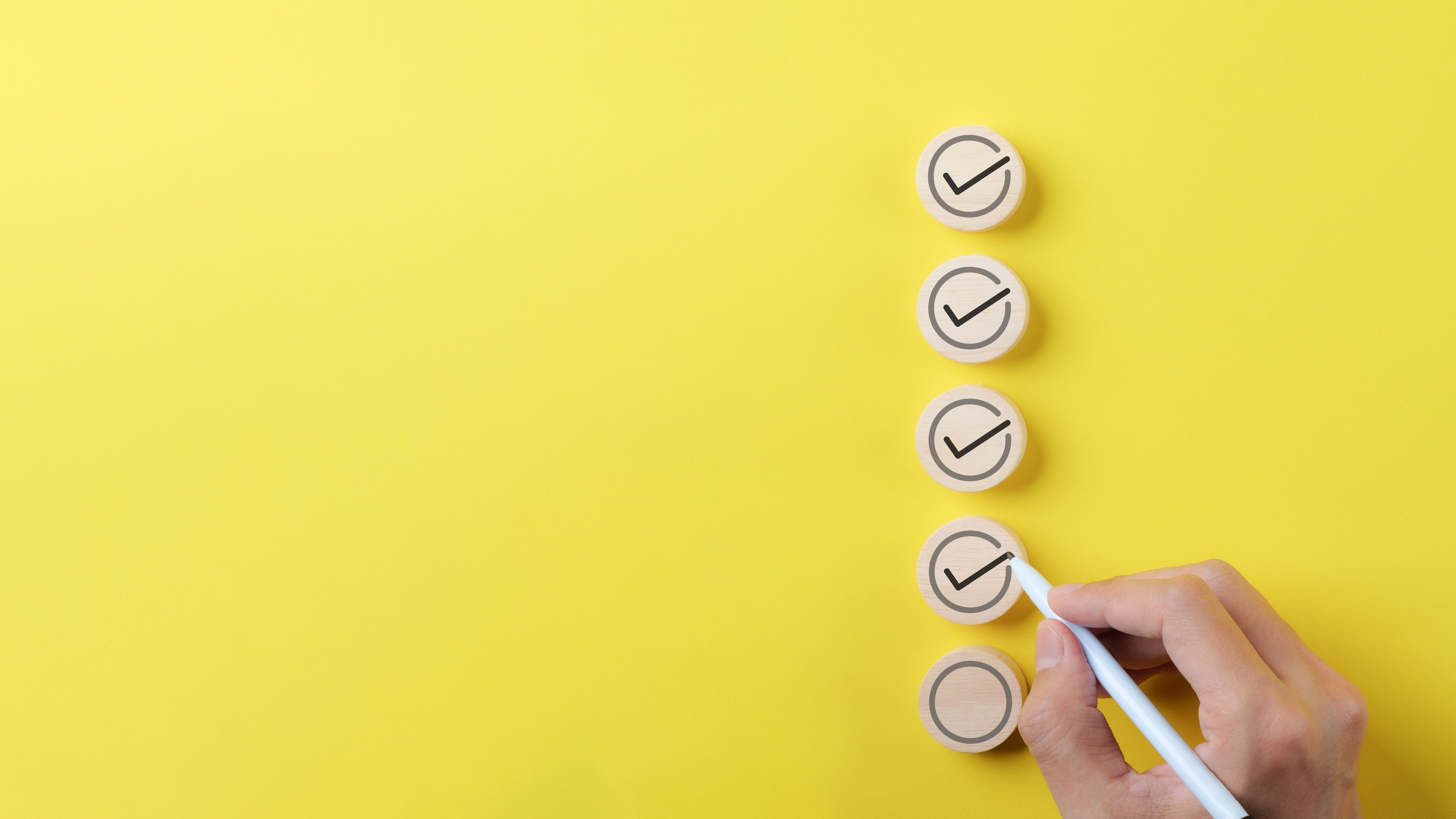 Checklist concept. Person using a black ink pen to correct sign and tick check mark on wooden block with copy space for the checklist on yellow background. Business survey questionnaire, exam process, Checklist concept. Person using a black ink pen to correct sign and tick check mark on wooden block with copy space for the checklist on yellow background. Business survey questionnaire, exam process,