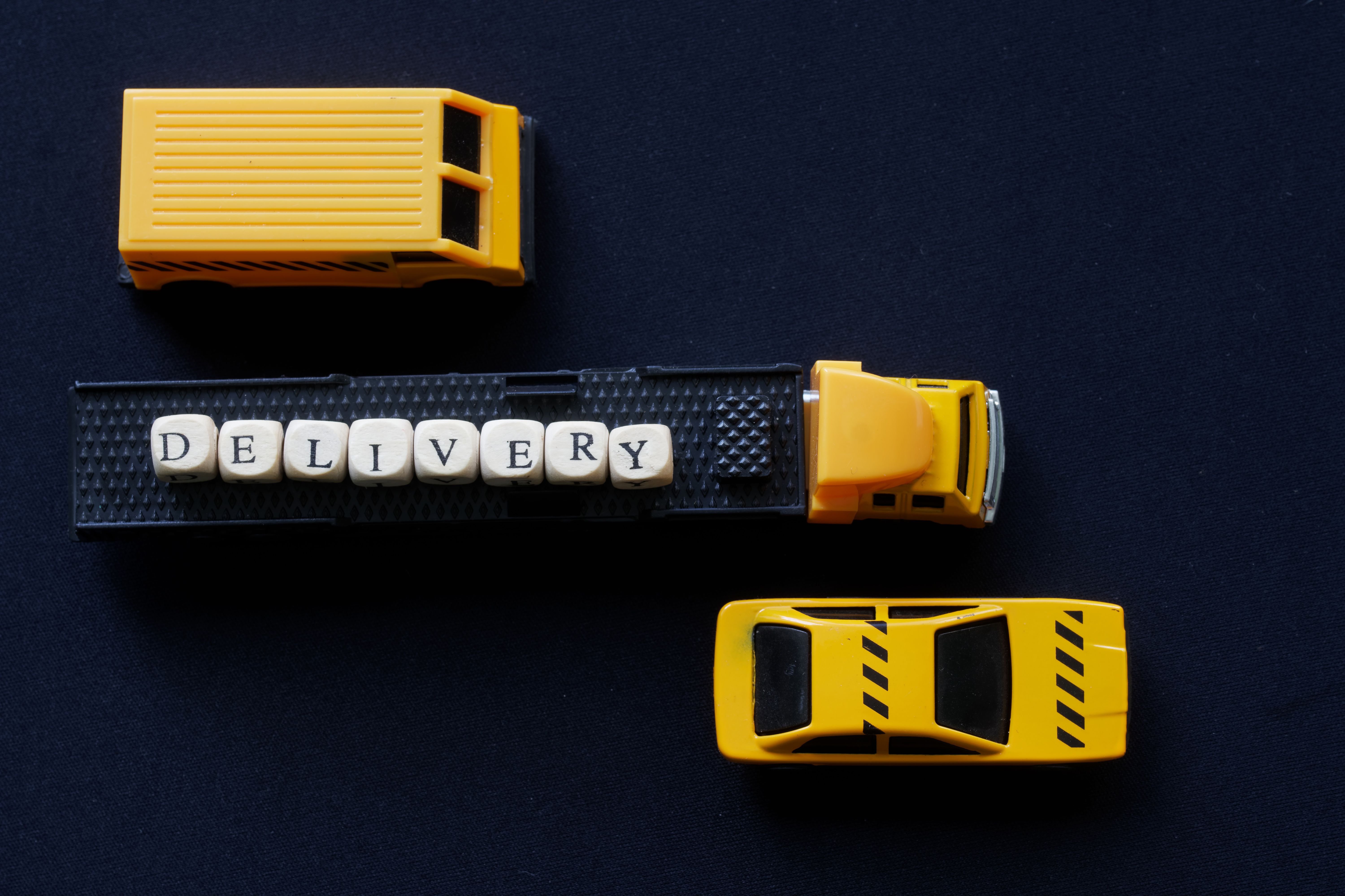 Yellow toy truck with a trailer and delivery among other vehicles. View from above. The concept of transportation and escorting the delivery of goods. Dark background Yellow toy truck with a trailer and delivery among other vehicles. View from above. The concept of transportation and escorting the delivery of goods. Dark background