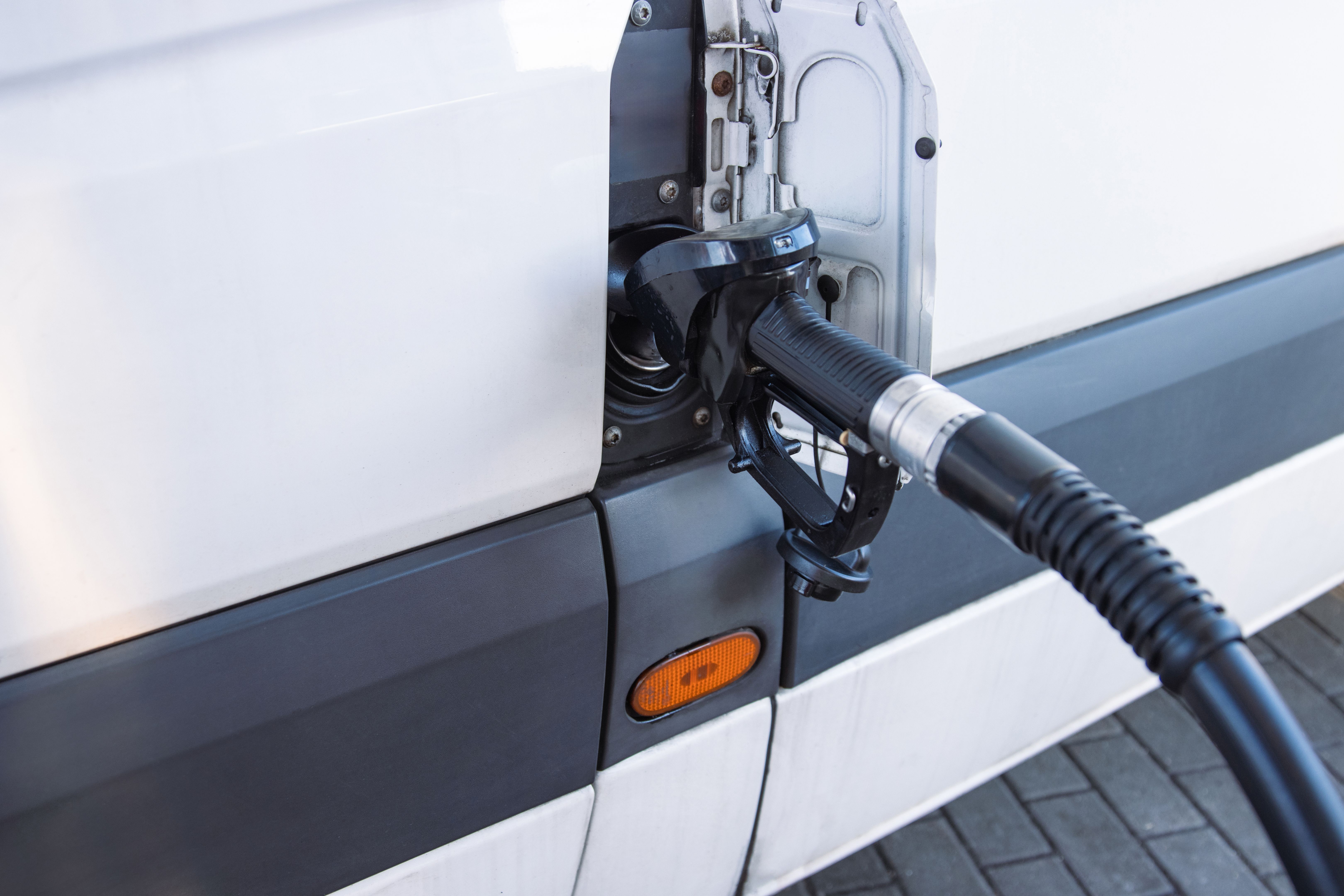 Closeup of a fuel nozzle in the car tank. Process of refilling a white transporter bus at a gas station. Refueling pistol inserted into a vehicle at a gas station. Copy space