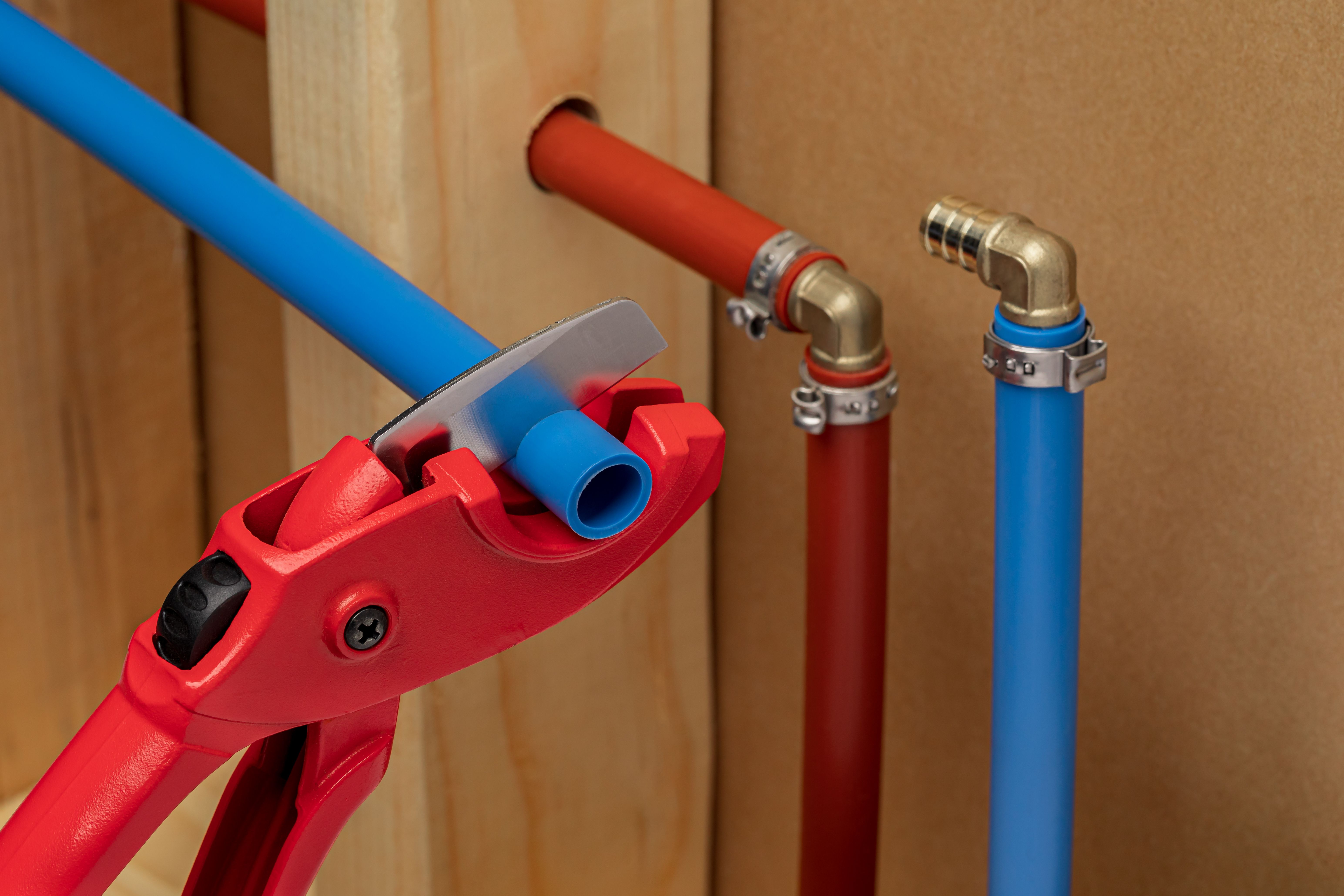 Cutting and installing PEX plastic water supply plumbing pipe in wall of house. Home repair, maintenance and remodeling concept.