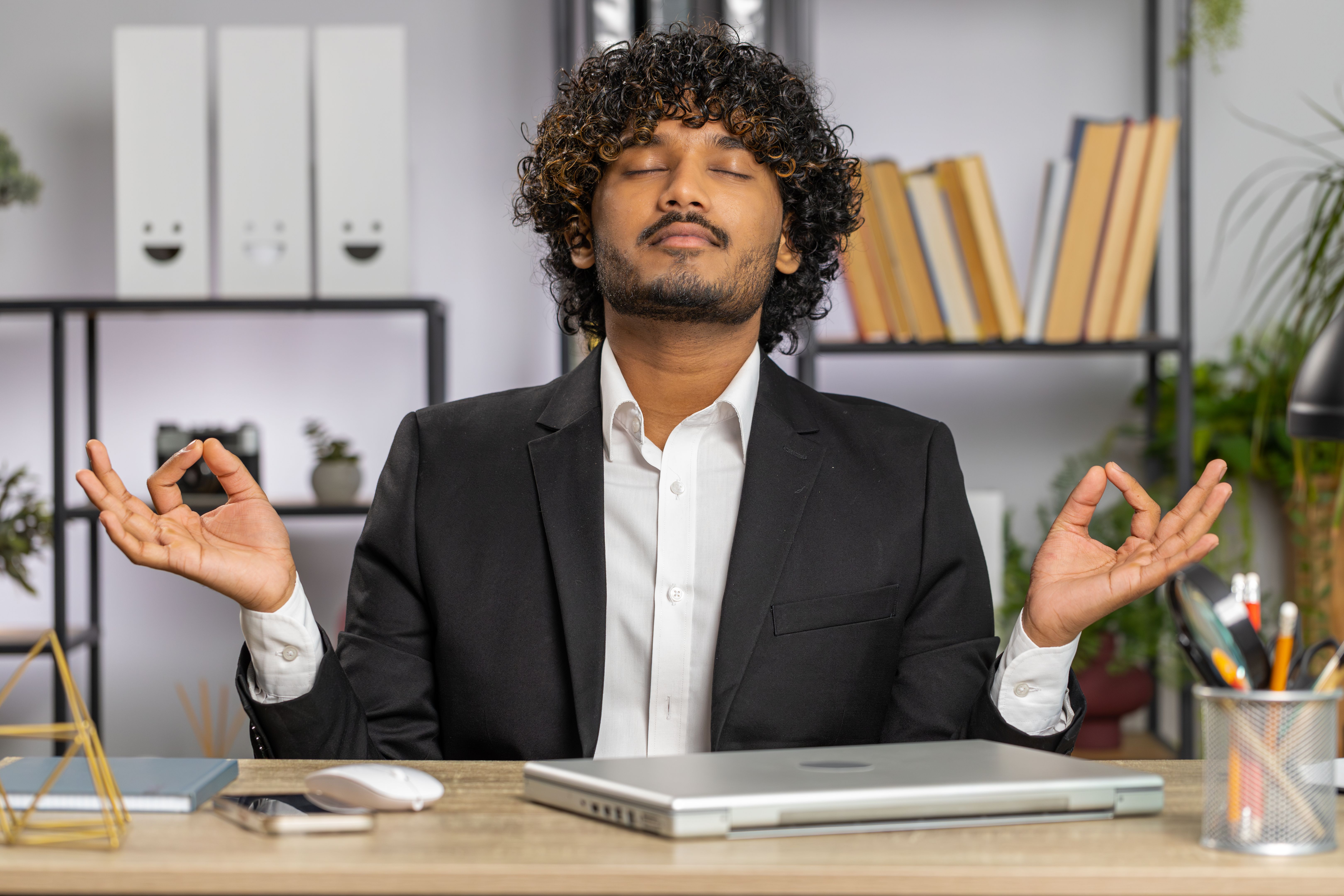 Businessman working on laptop, meditating, doing yoga breathing exercise in lotus position at office