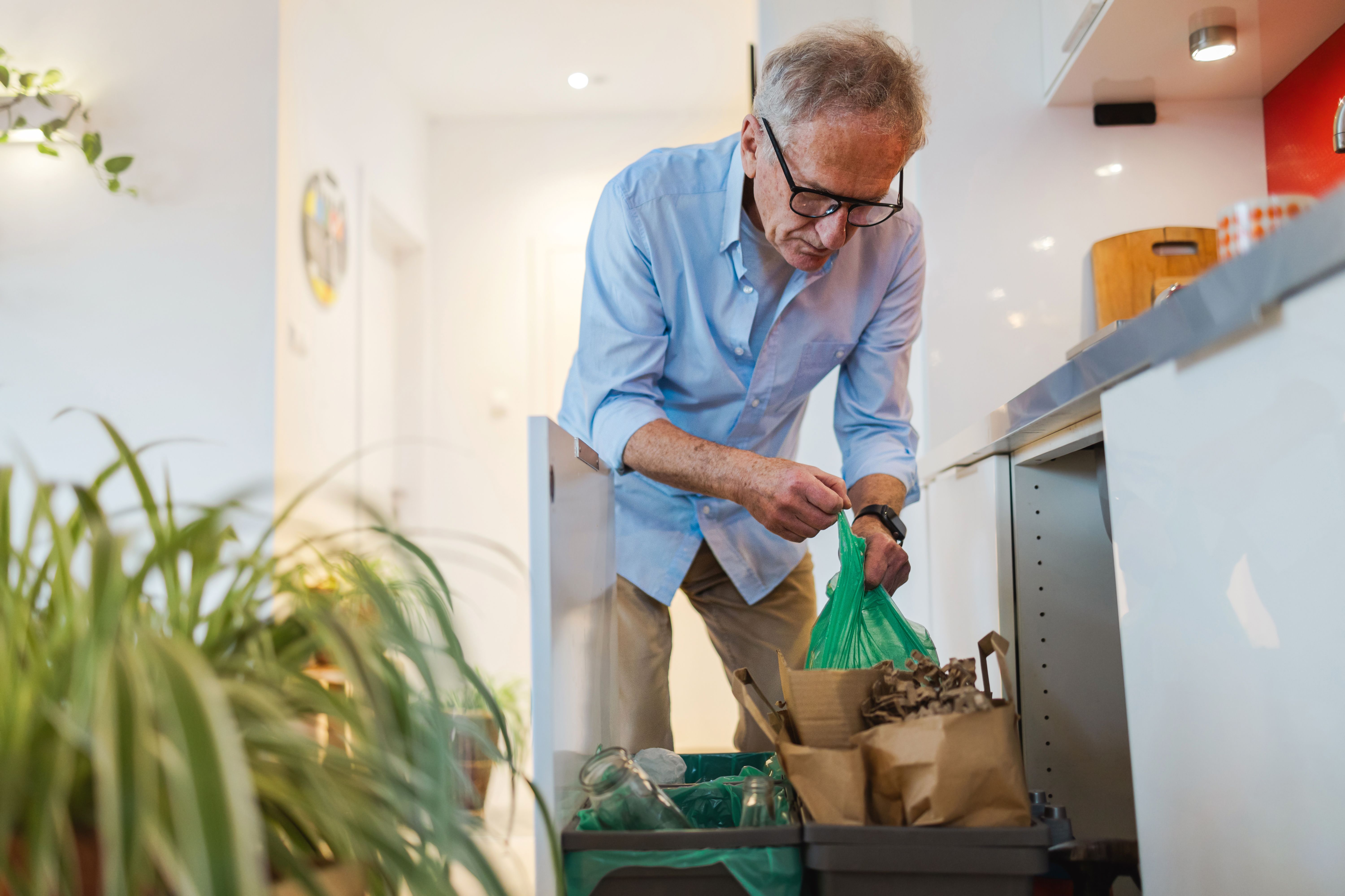 Älterer Mann sortiert zu Hause Müll in Recycling-Behältern Älterer Mann sortiert zu Hause Müll in Recycling-Behältern