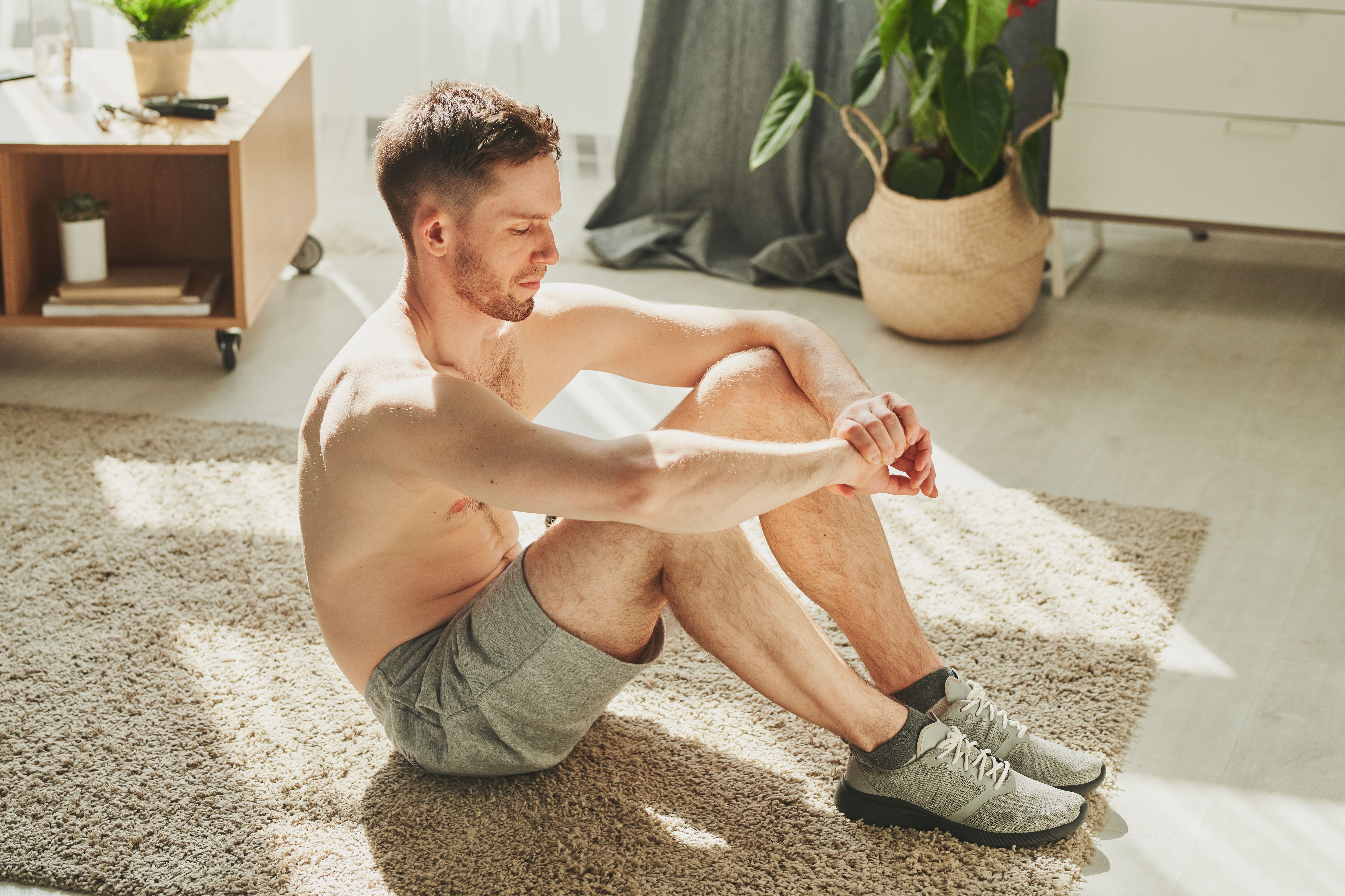 Shirtless athlete having rest on the floor of living-room after hard training