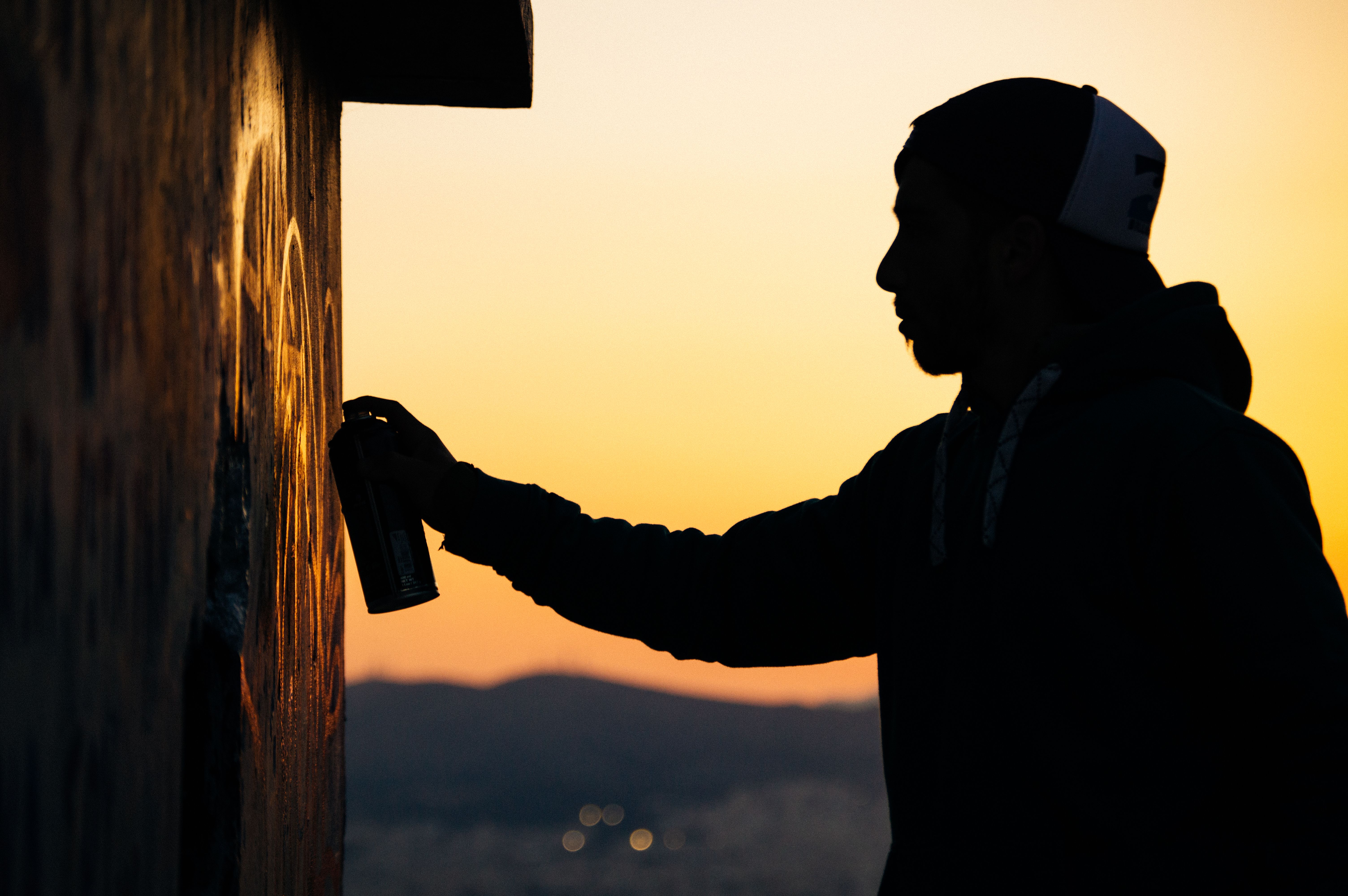 Silhouette eines Graffiti Künstlers beim Sprayen an einer Wand im Sonnenuntergang Silhouette eines Graffiti Künstlers beim Sprayen an einer Wand im Sonnenuntergang
