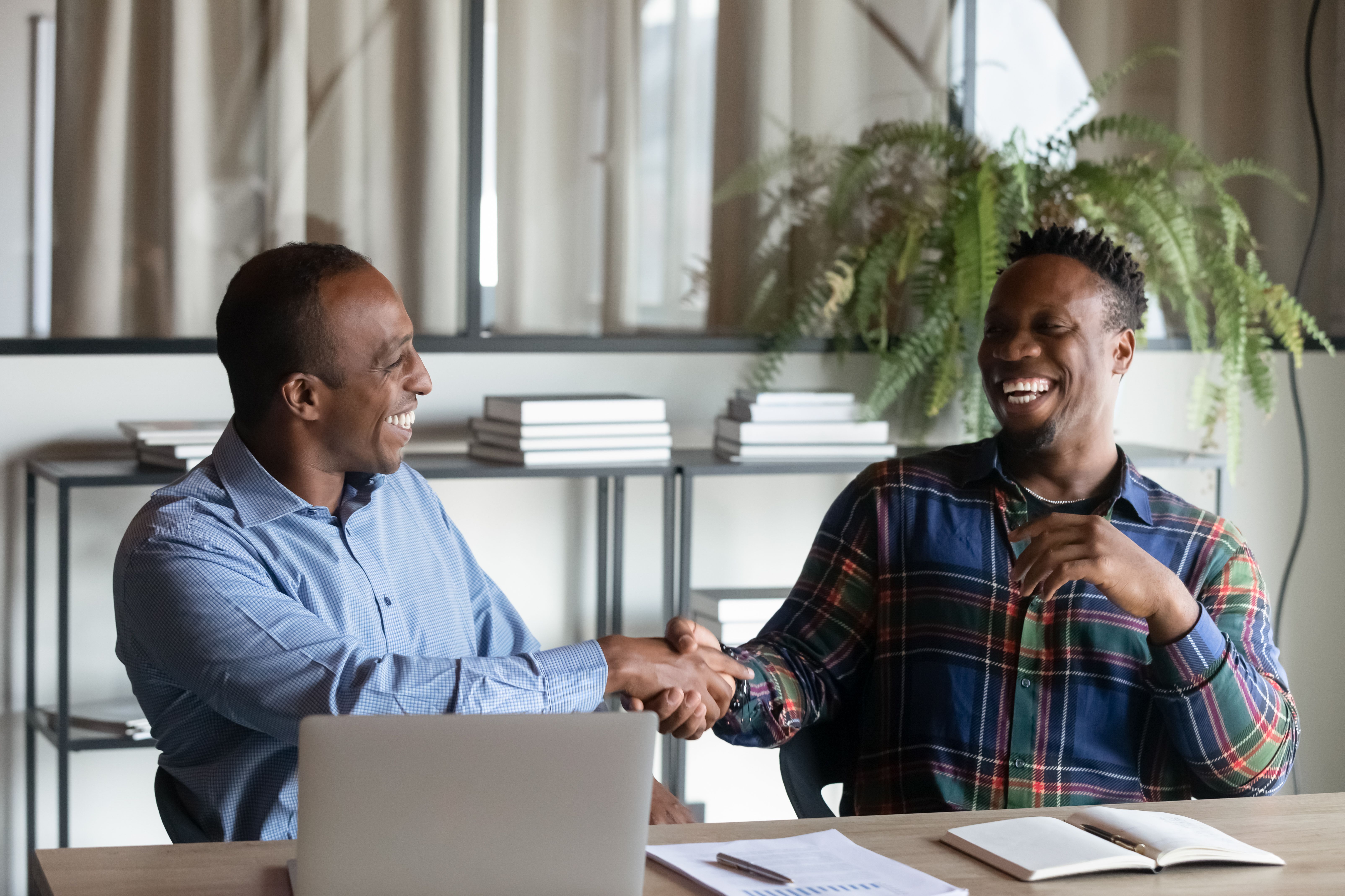 Smiling ethnic male colleagues handshake at office meeting Smiling ethnic male colleagues handshake at office meeting
