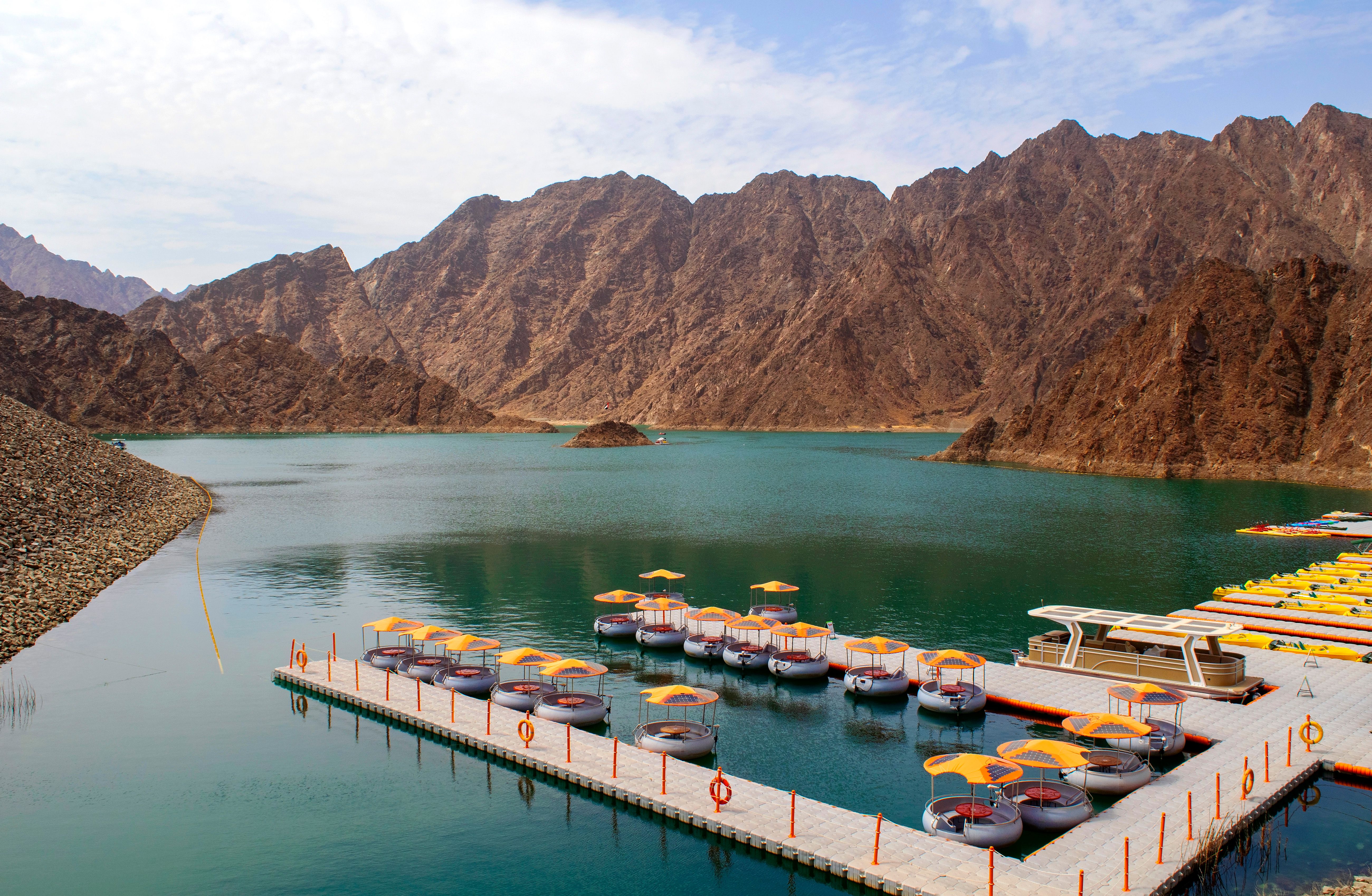 Beautiful deep green Hatta lake between Hajar Mountains with many kayaks and boats for rent