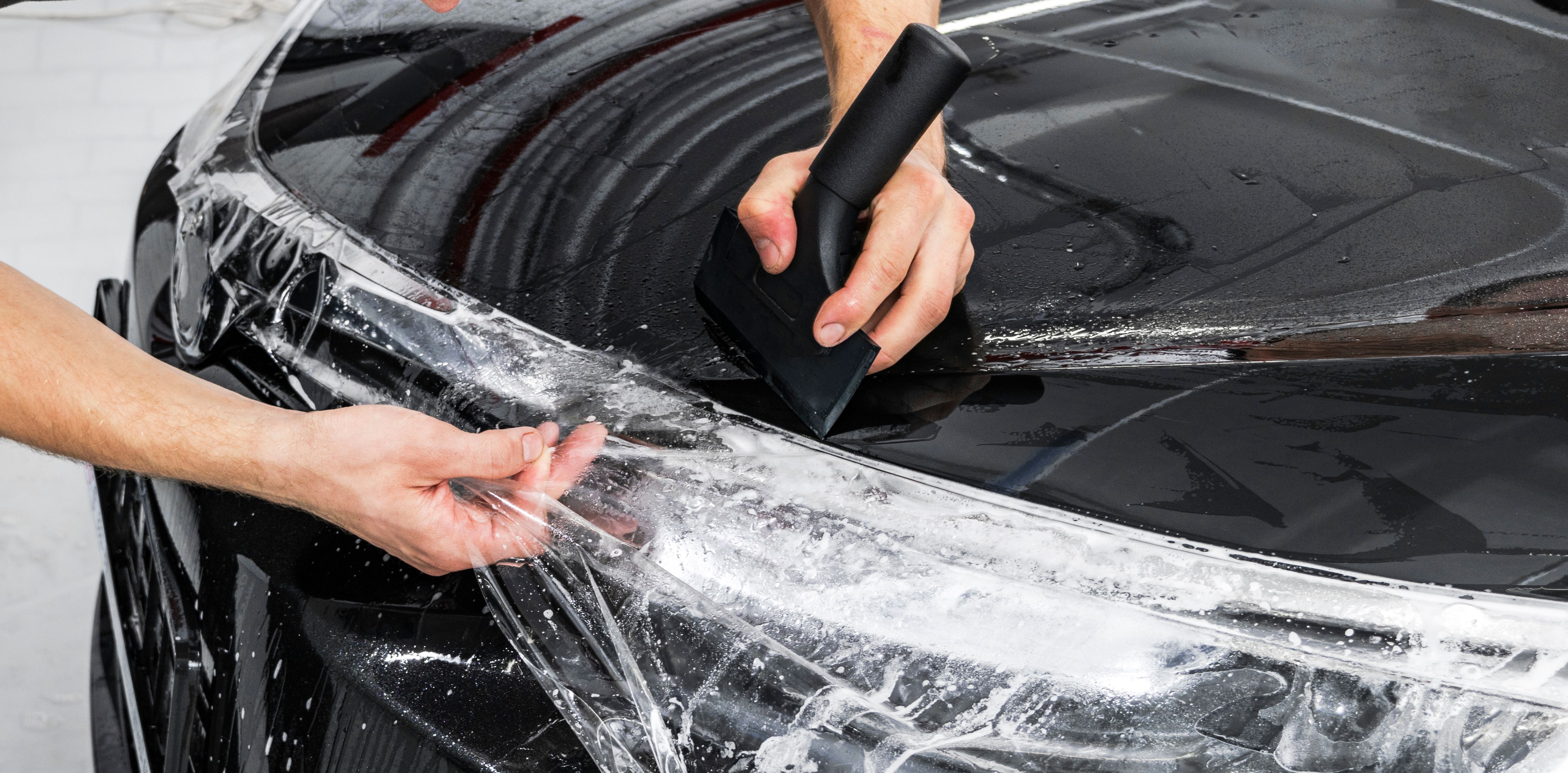 Car wrapping specialist putting vinyl foil or film on car. Protective film on the car. Applying a protective film to the car with tools. Car detailing. Transparent film. Car paint protection. Trimming