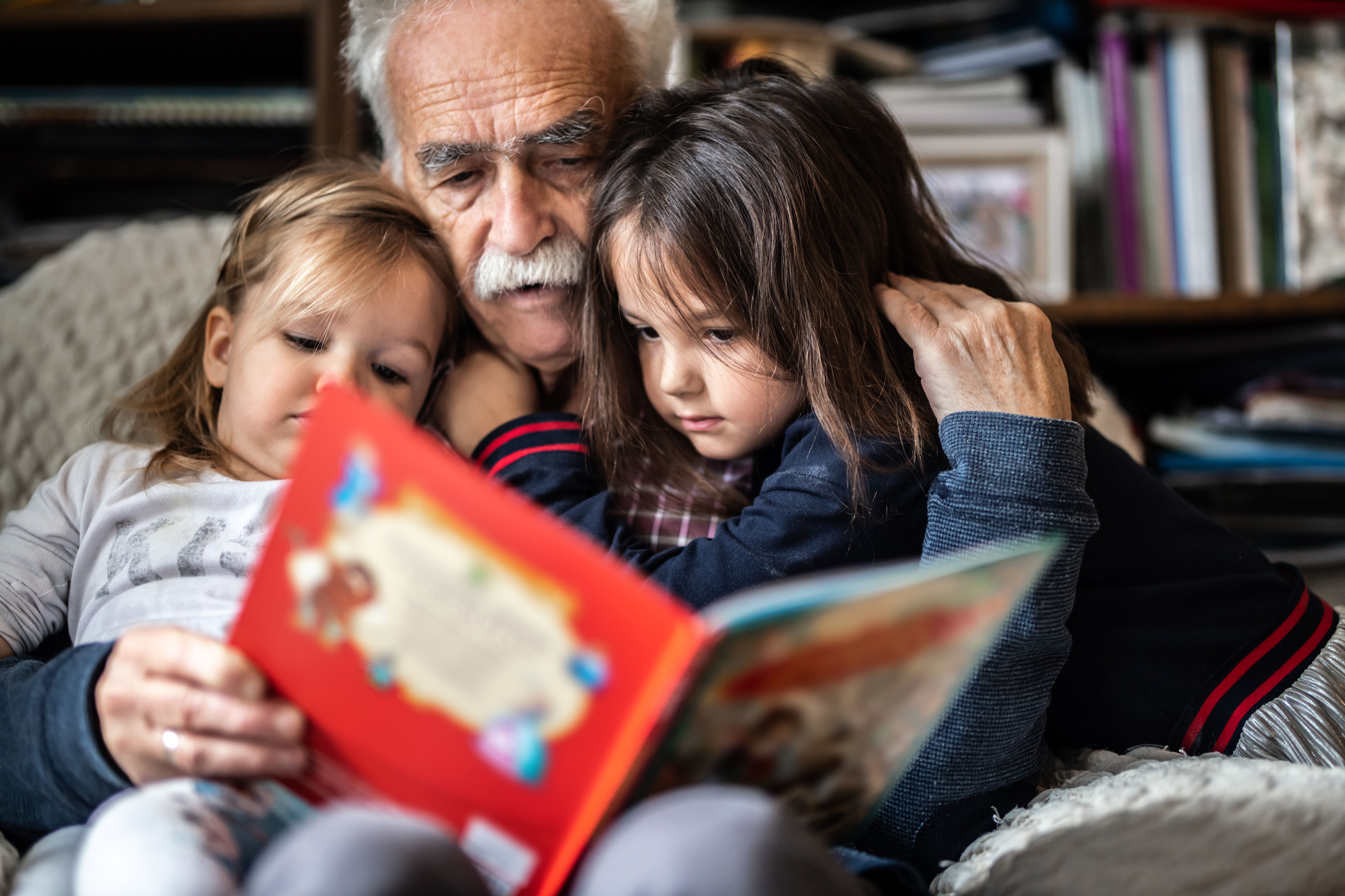 Adorable little girls reading kids book with Grandpa