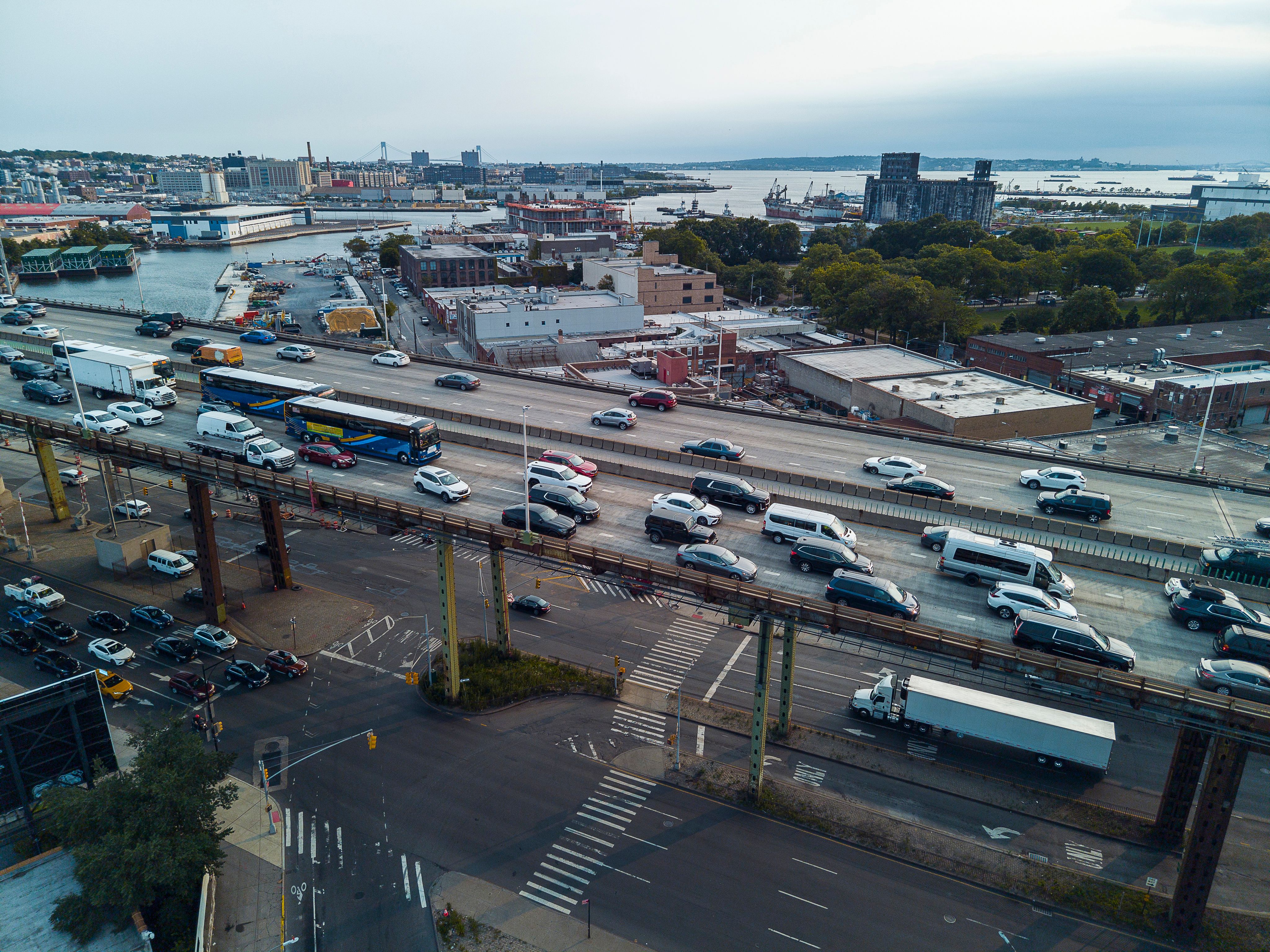 Elevated Belt Parkway with heavy traffic in the evening in Brooklyn. Gowanus Canal and Expressway under Belt Parkway, traffic, and distant industrial districts of Brooklyn. Drone view