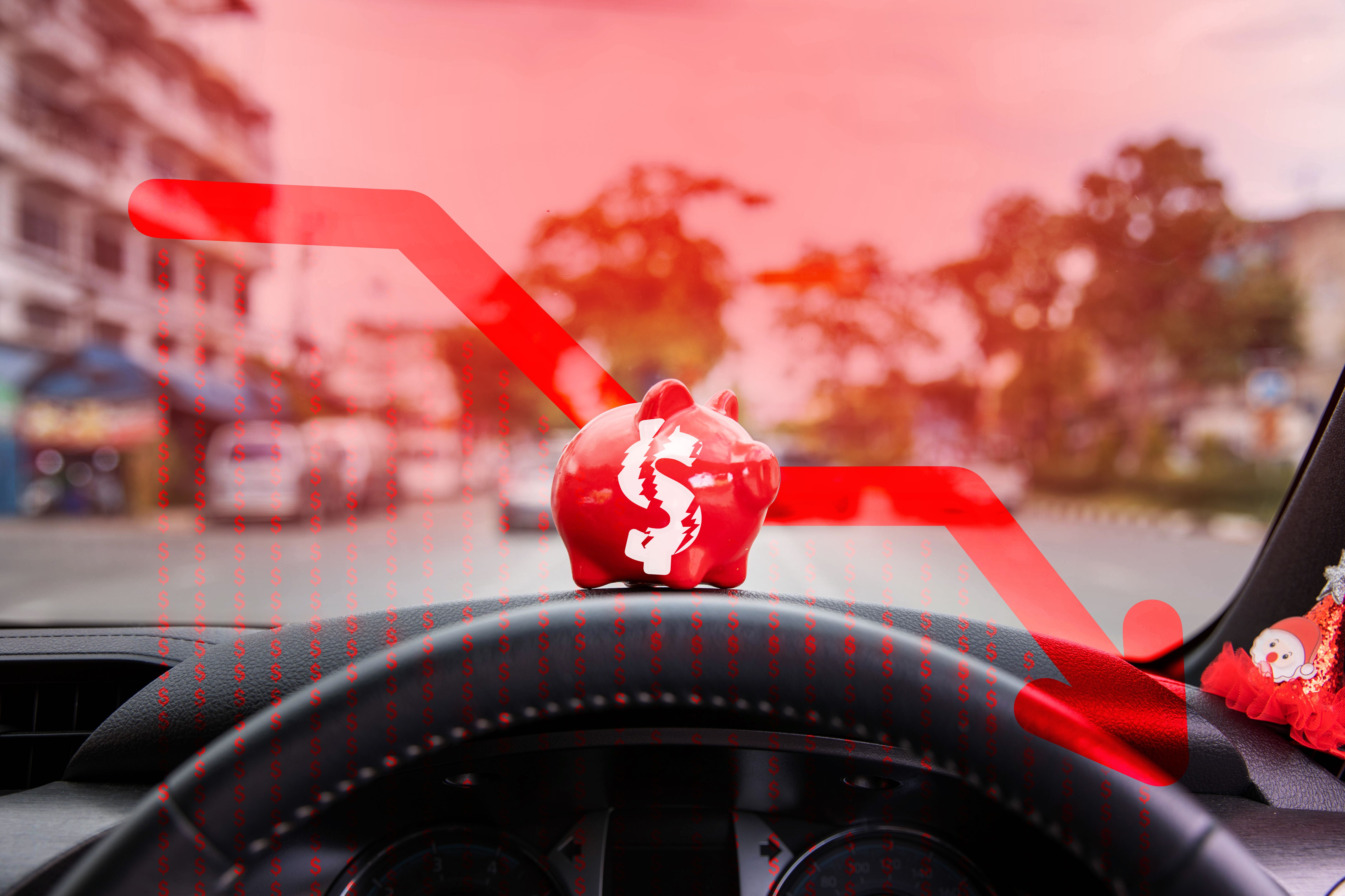 A red piggy bank is placed on the car's console, and the financial graph is deteriorating, lack of liquidity, and debt.