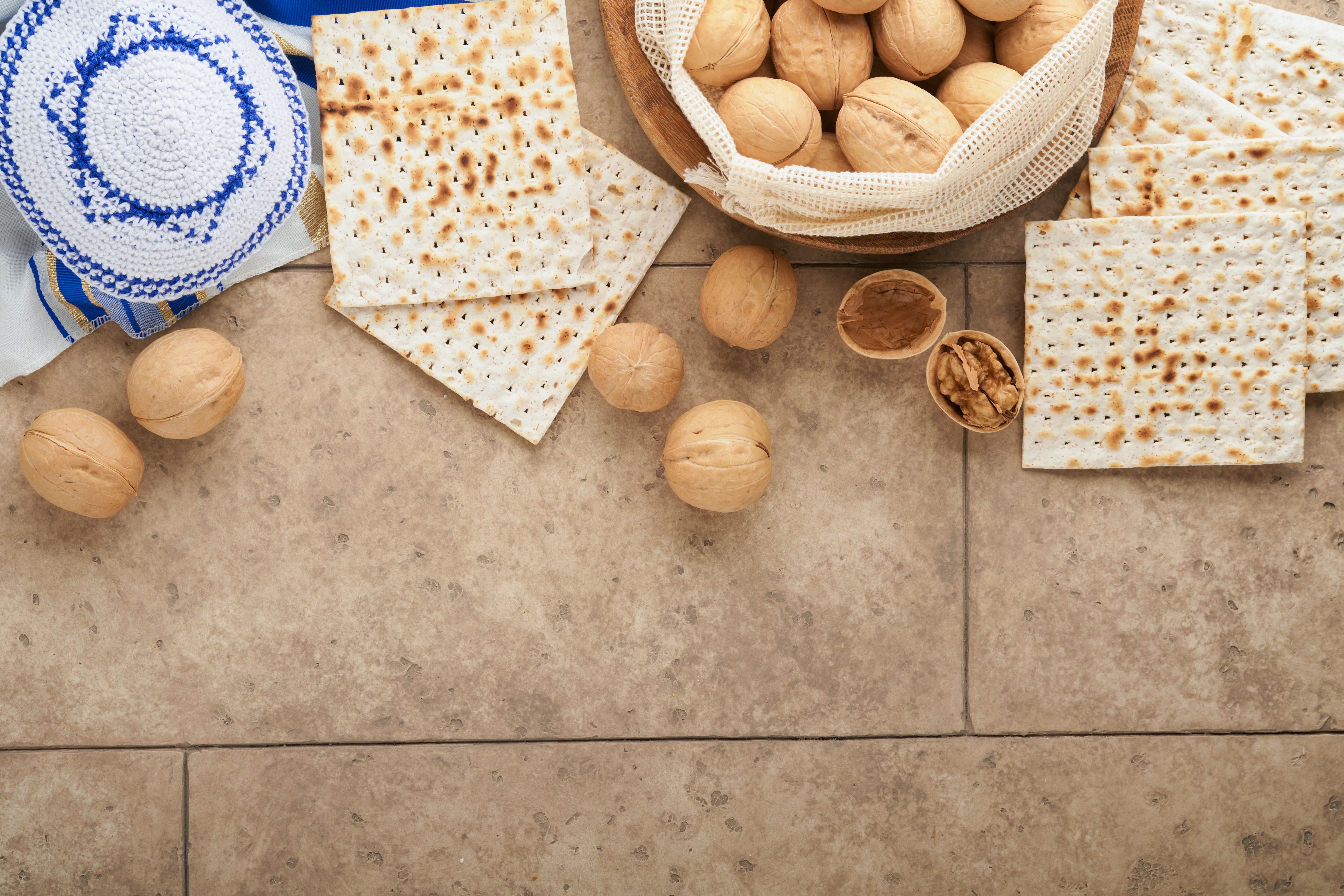 Passover celebration concept. Matzah, red kosher and walnut. Traditional ritual Jewish bread matzah, kippah and tallit on old concrete background. Passover food. Pesach Jewish holiday.