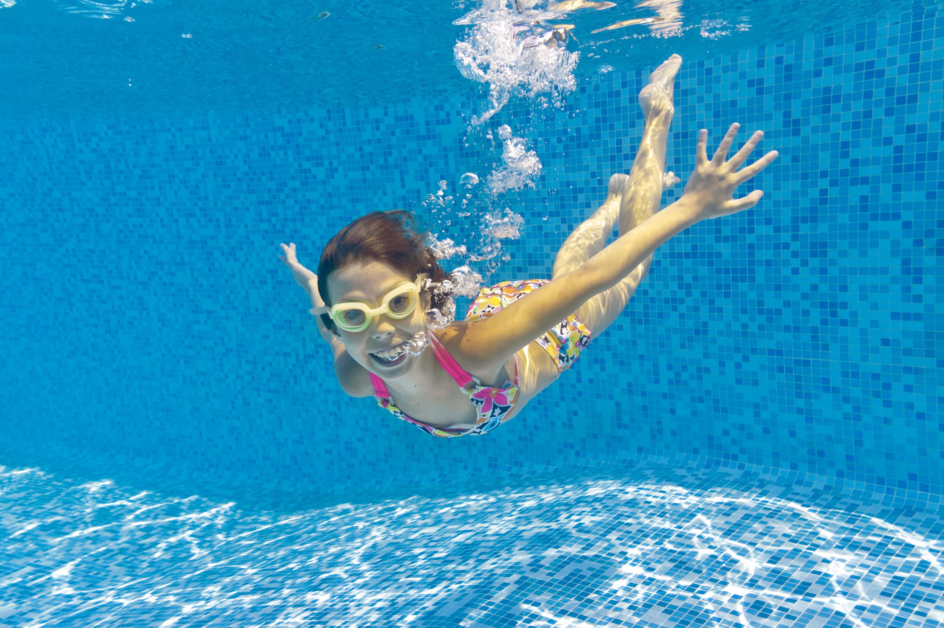 A smiling child swimming underwater in a pool in goggles