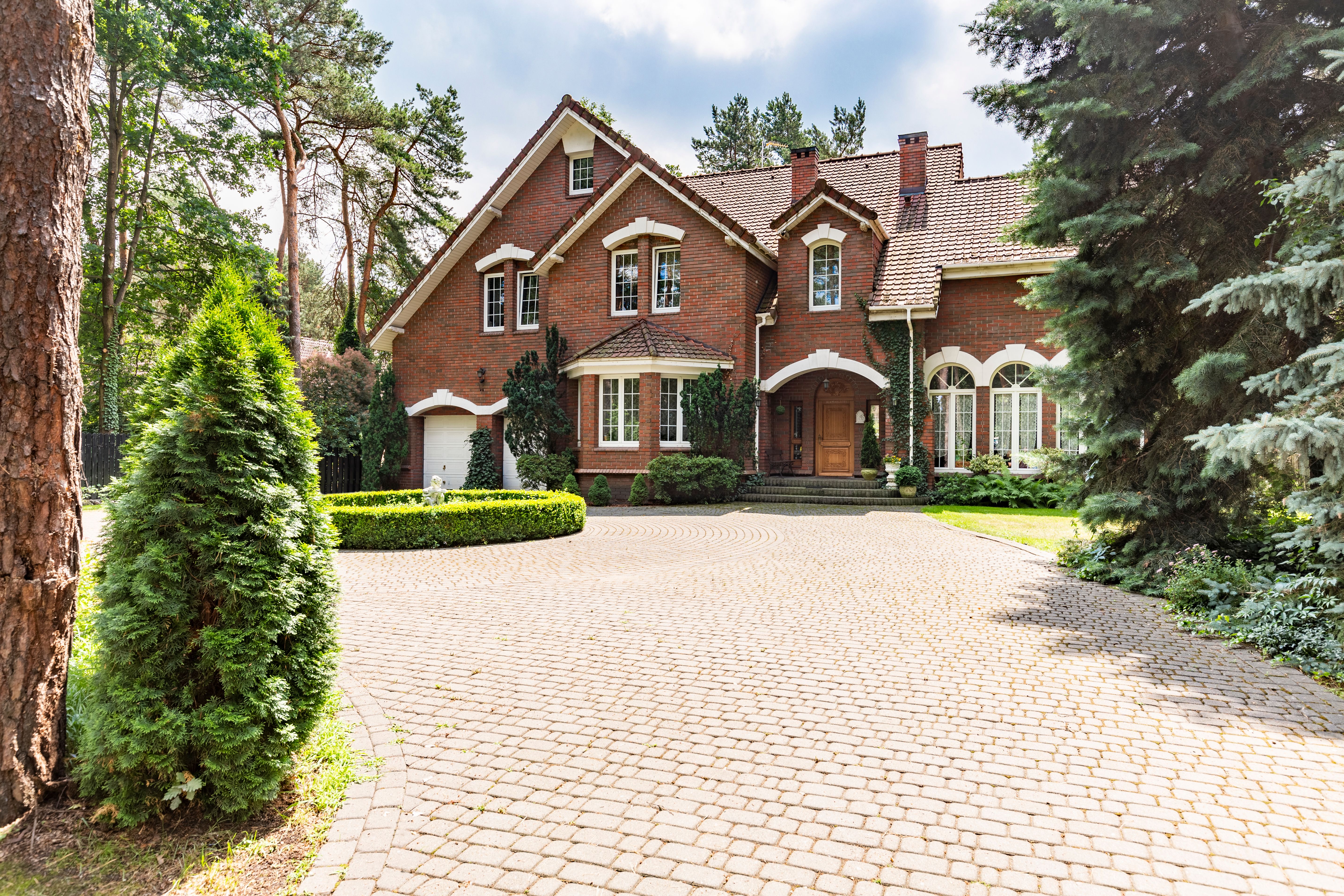 Large cobbled driveway in front of an impressive red brick English design mansion surrounded by old trees Large cobbled driveway in front of an impressive red brick English design mansion surrounded by old trees