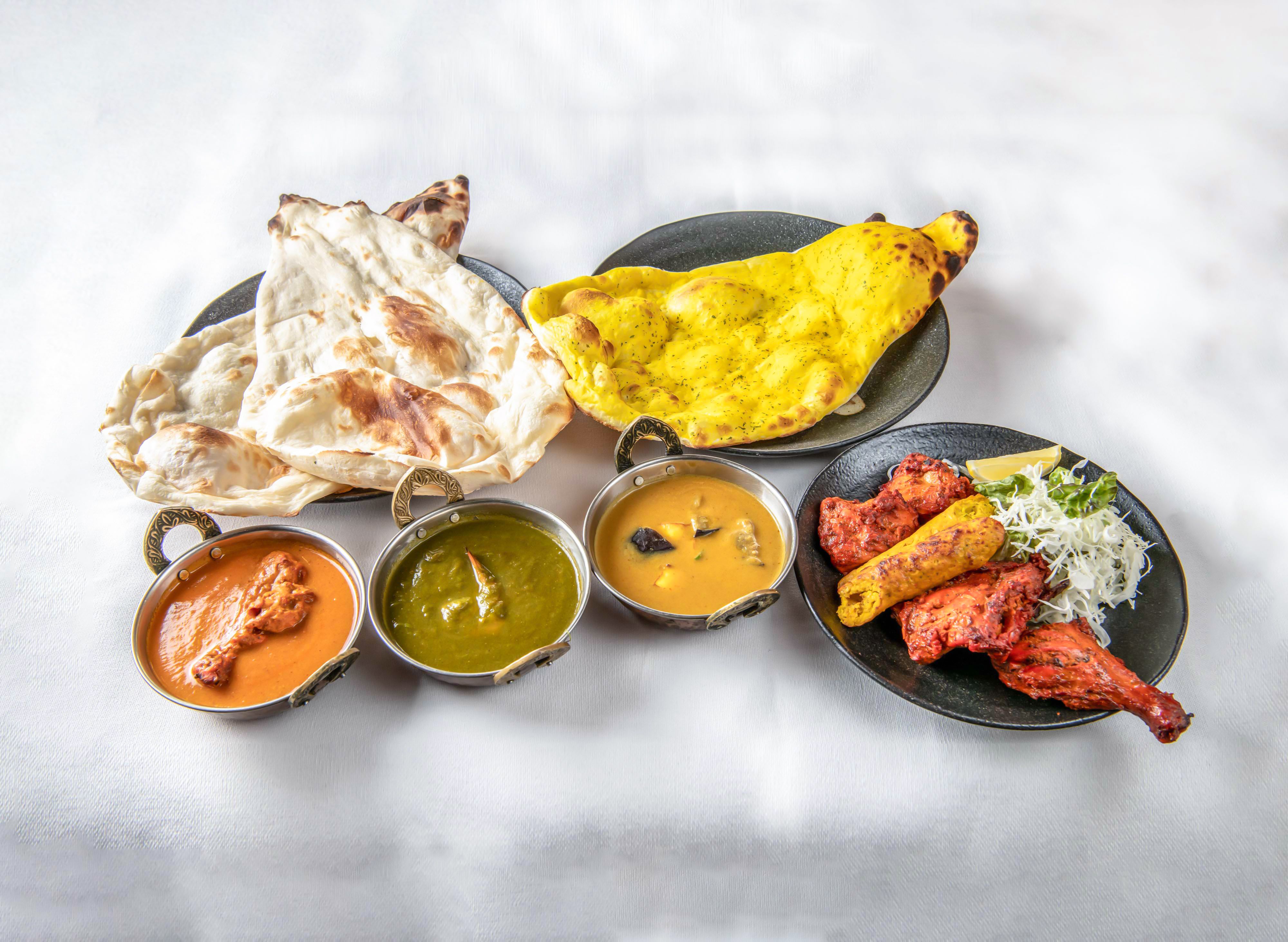 Indian food Set with Naan bread, Tandoori Chicken, kebab, Saag Curry, baingan and Chicken Curry on a White background side view of indian food Indian food Set with Naan bread, Tandoori Chicken, kebab, Saag Curry, baingan and Chicken Curry on a White background side view of indian food