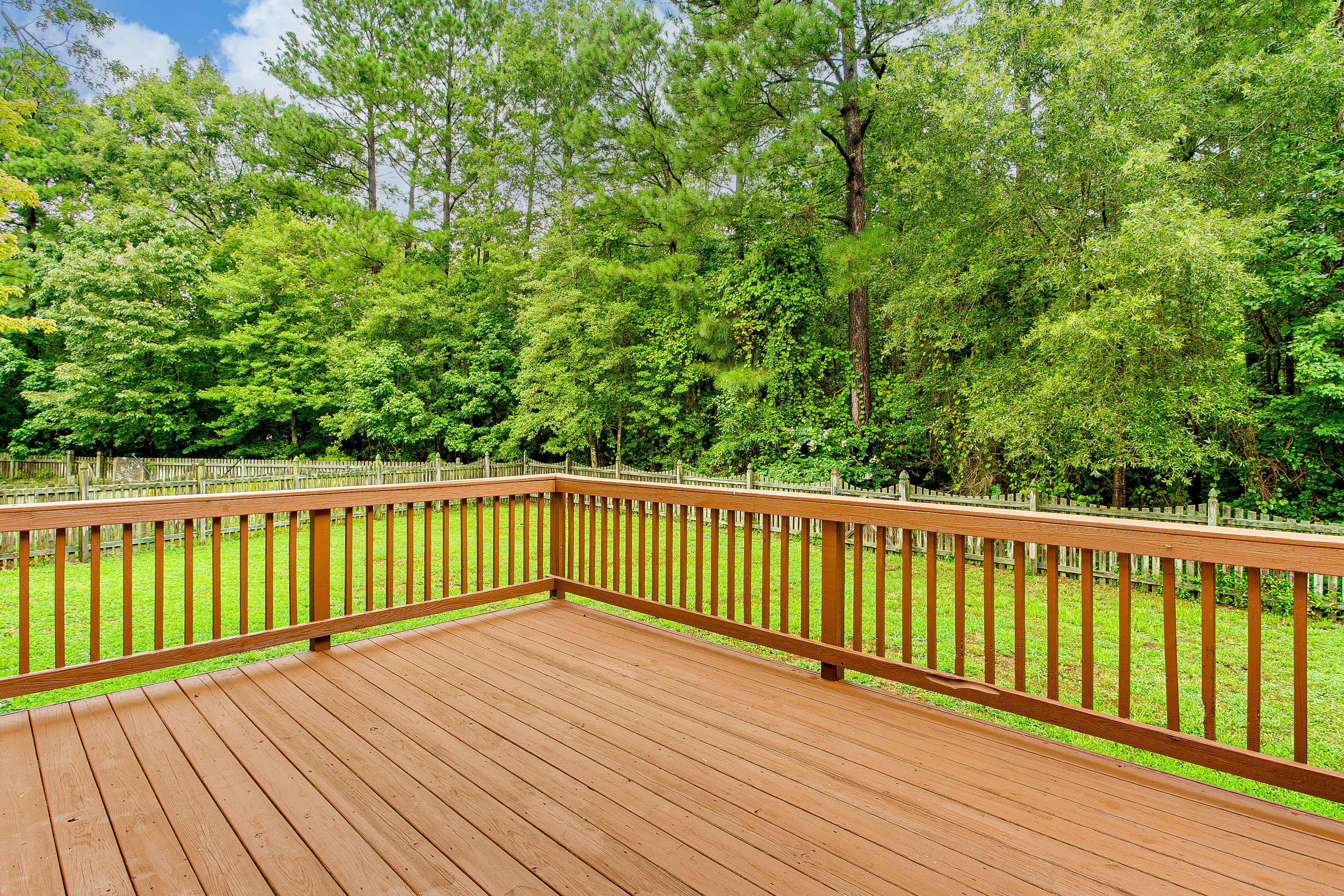 Sunny Wooden Deck With Railing Overlooking Lush Green Backyard in Summer