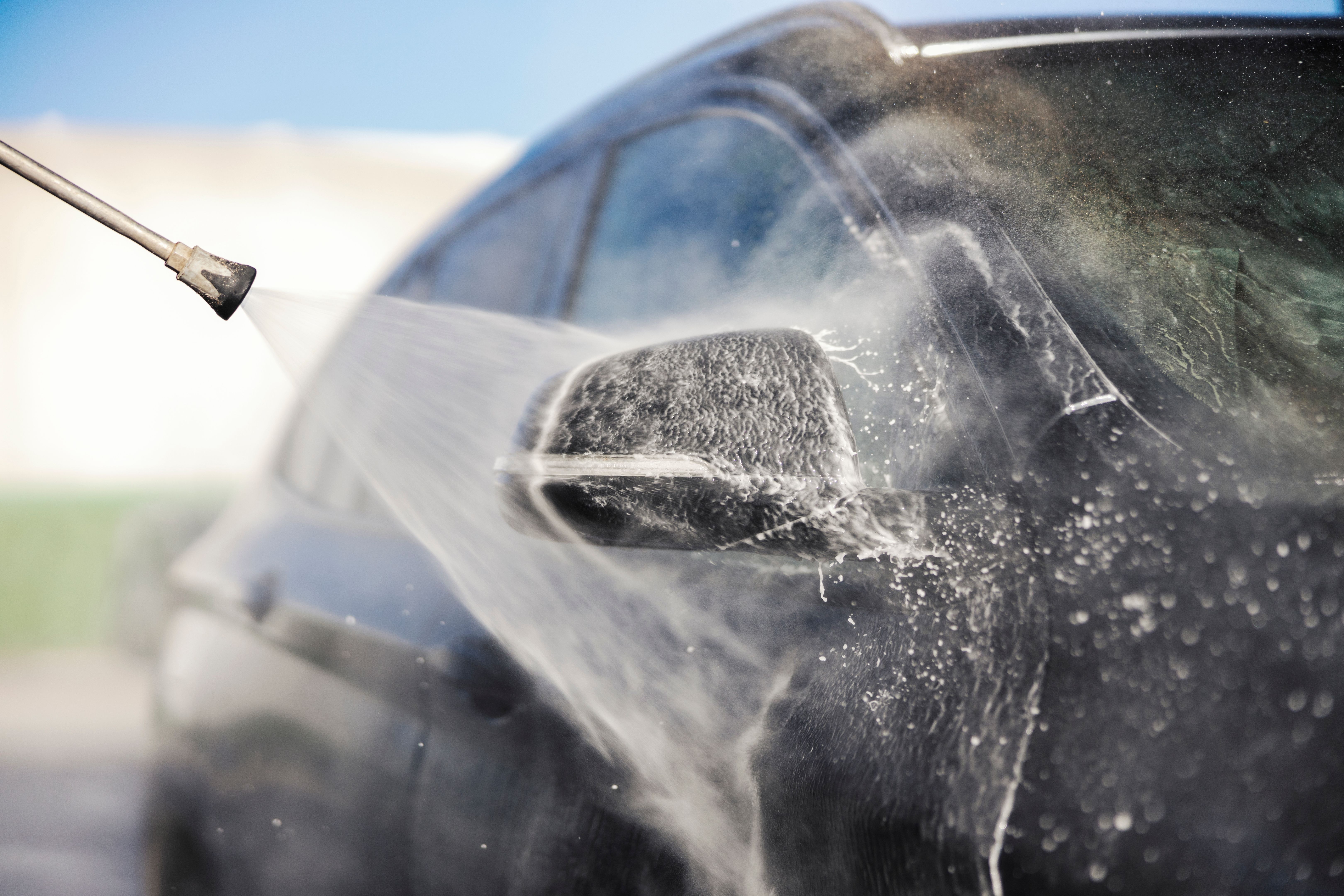 Close up of high pressure water gun cleaning car at carwash station.