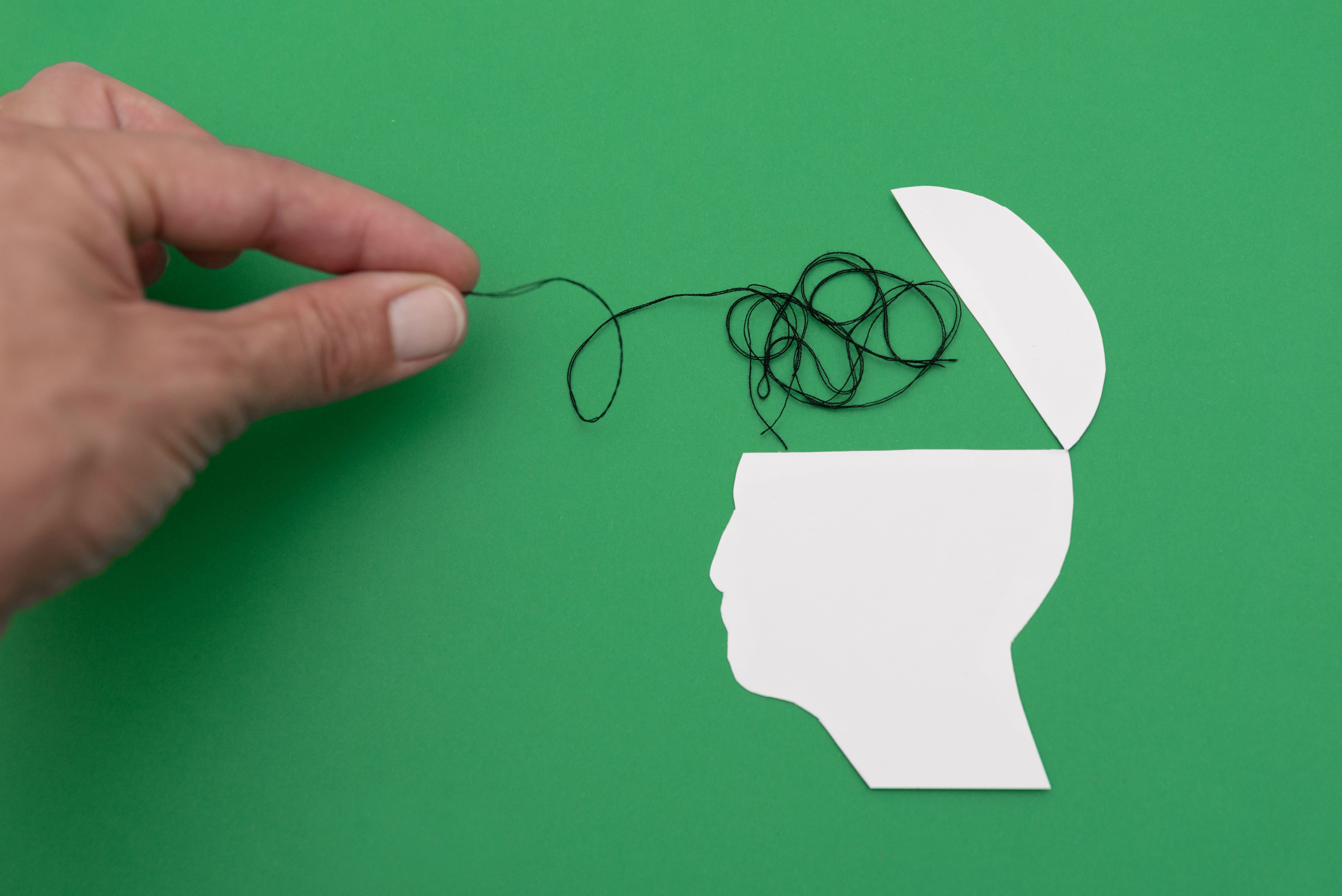 Hand pulling tangled thread from an open white head silhouette on green background symbolizing problem-solving and mental health Hand pulling tangled thread from an open white head silhouette on green background symbolizing problem-solving and mental health