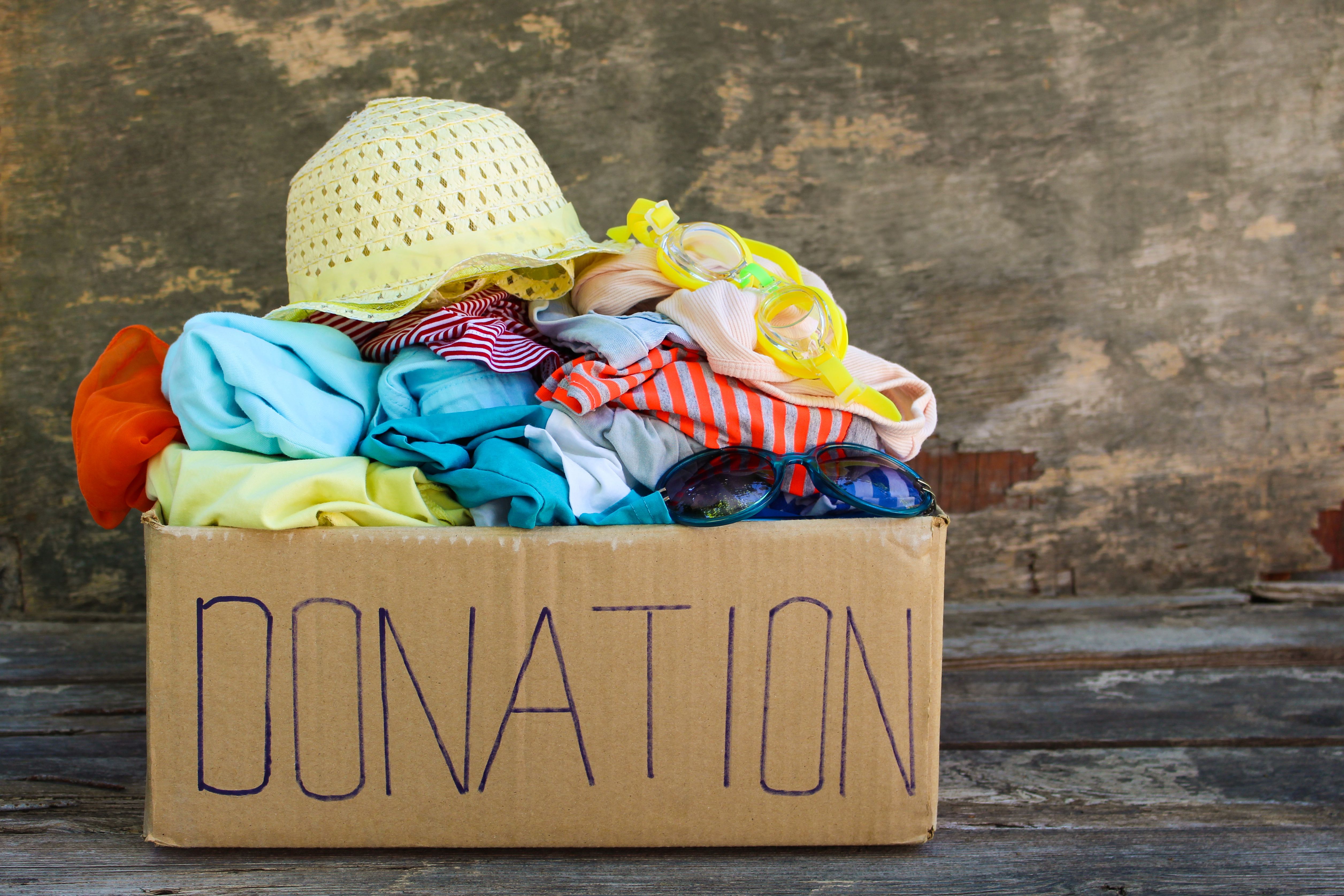 Donation box with summer clothes on the old wooden background. Donation box with summer clothes on the old wooden background.