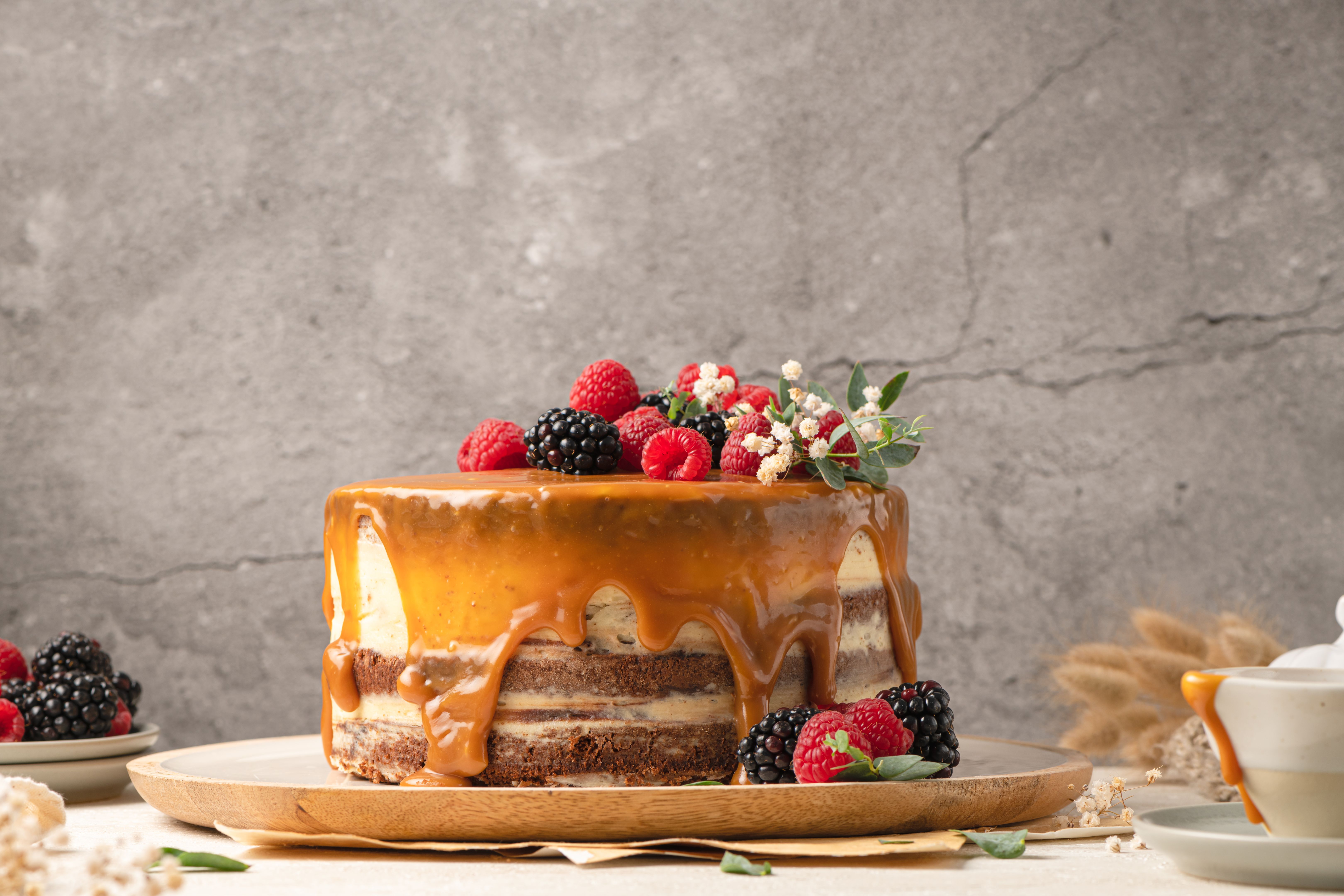 Delicious chocolate cake topped with mascarpone cream and salted caramel. Decorated with red fruits. Light background