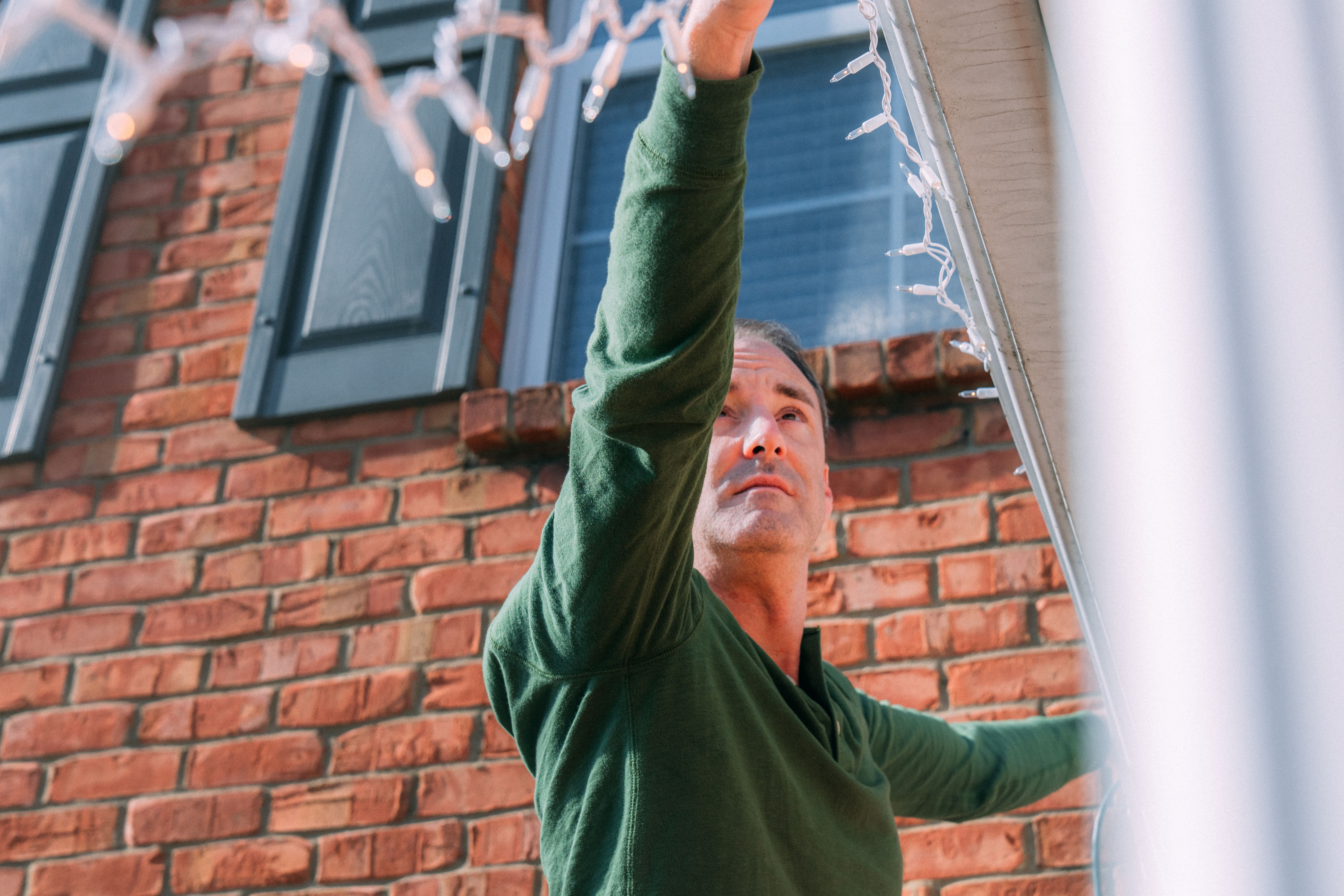 Low Angle Close-Up Shot of a Man Hanging Christmas Lights on the House Gutters, Decorating for Christmas Holiday