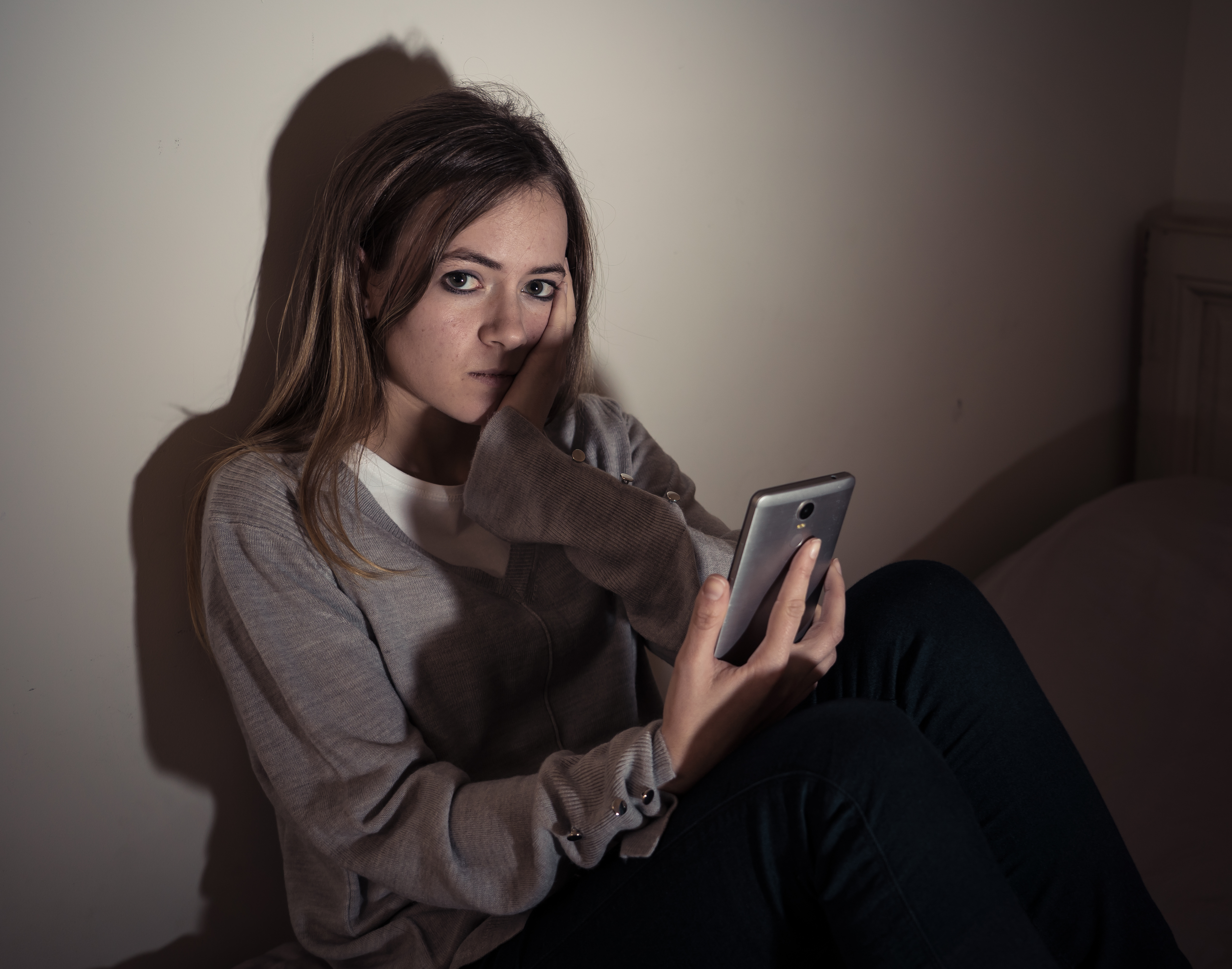 Young teenager girl suffering mobile cell phone addiction feeling lonely and depressed having insomnia needing to be connected sitting on bed late at night. In internet and mobile addiction concept.