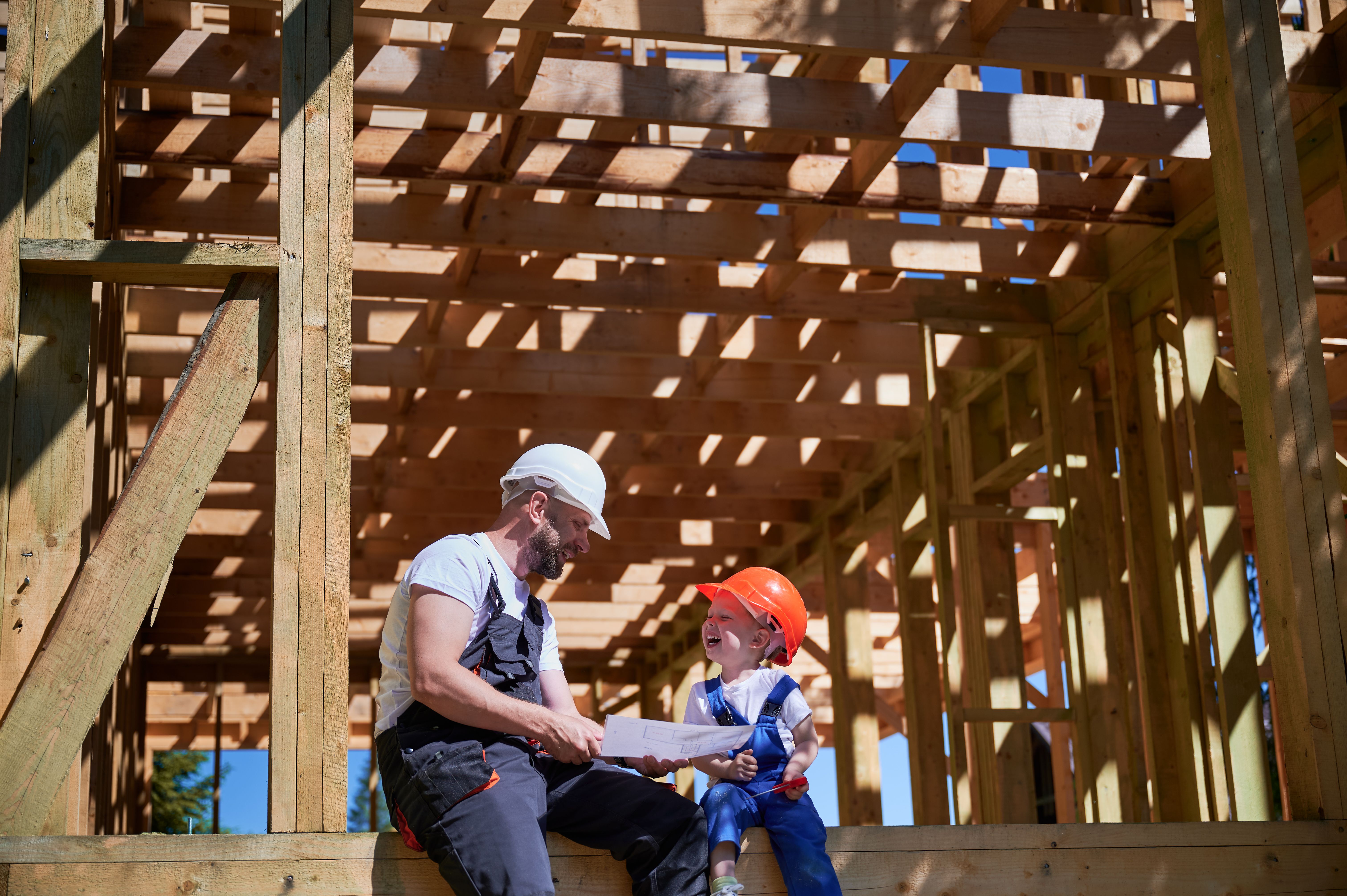 Father teaching his toddler son the art building wooden frame house on construction site.