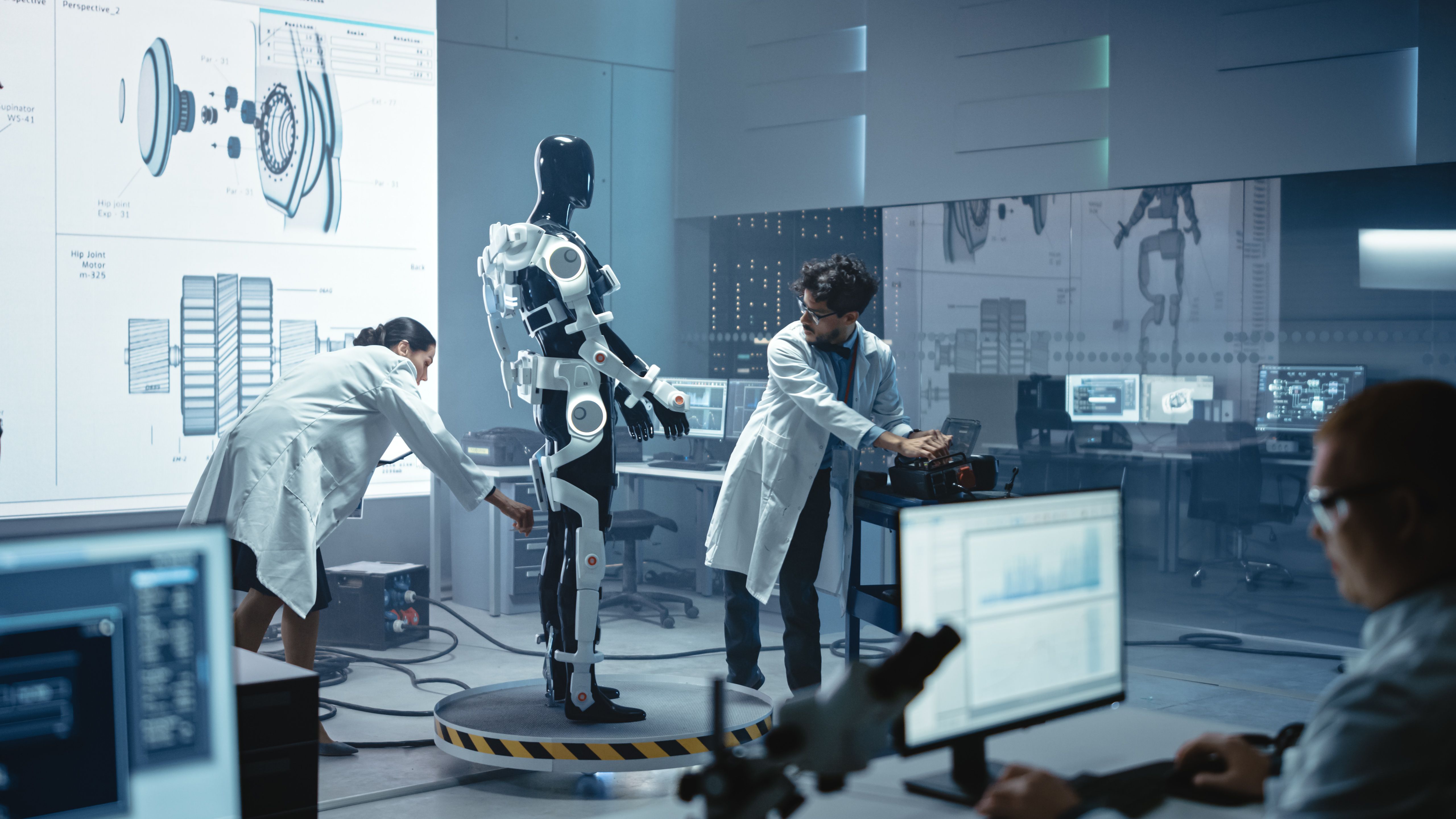 In Robotics Development Laboratory: Chief Female Engineer and Top Male Scientist Work on a Bionics Exoskeleton Prototype. Designing Powered Exosuit to Help Disabled People, Hard Labor Workers