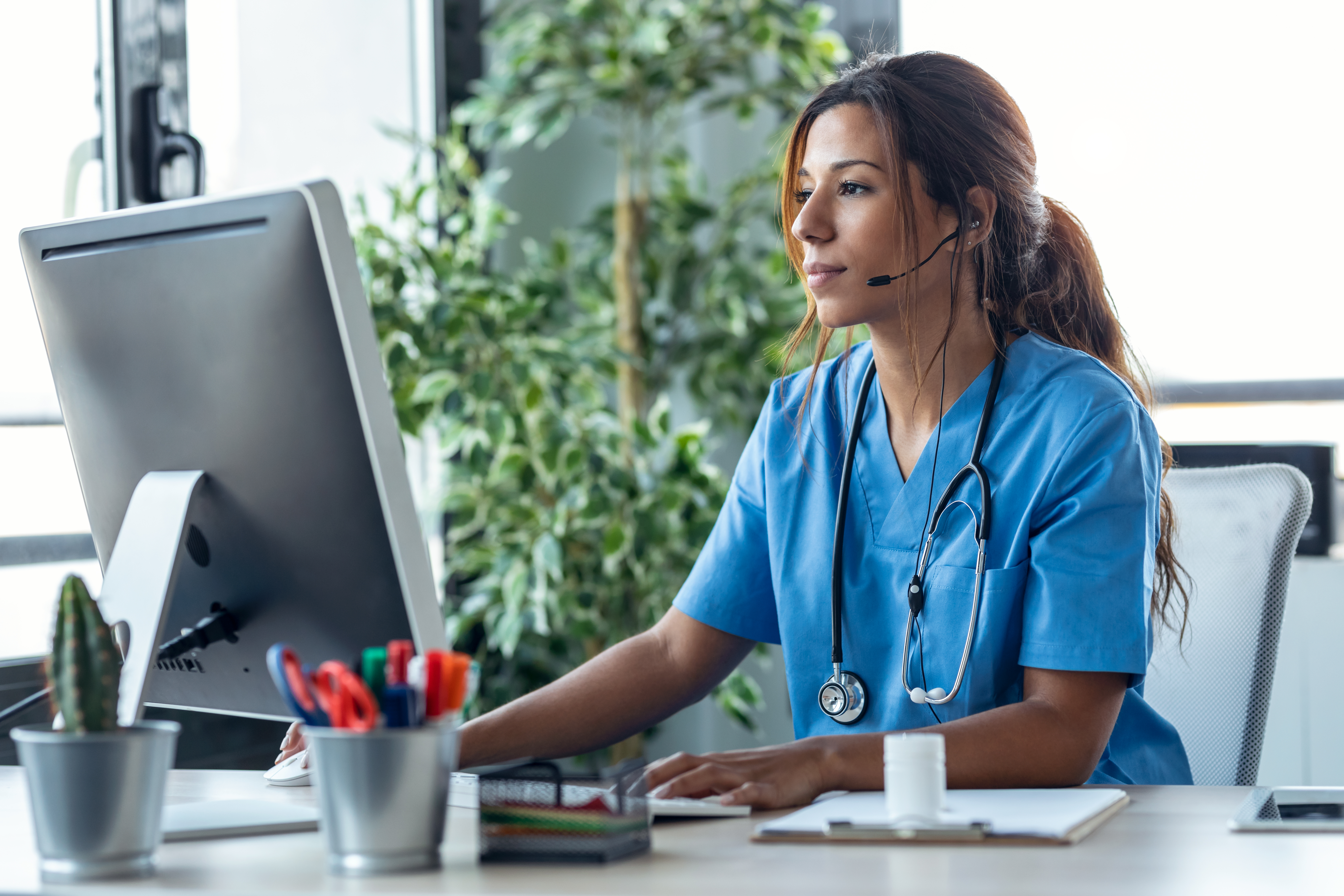 Female doctor talking with earphone while explaining medical treatment to patient through a video call with computer in the consultation. Female doctor talking with earphone while explaining medical treatment to patient through a video call with computer in the consultation.