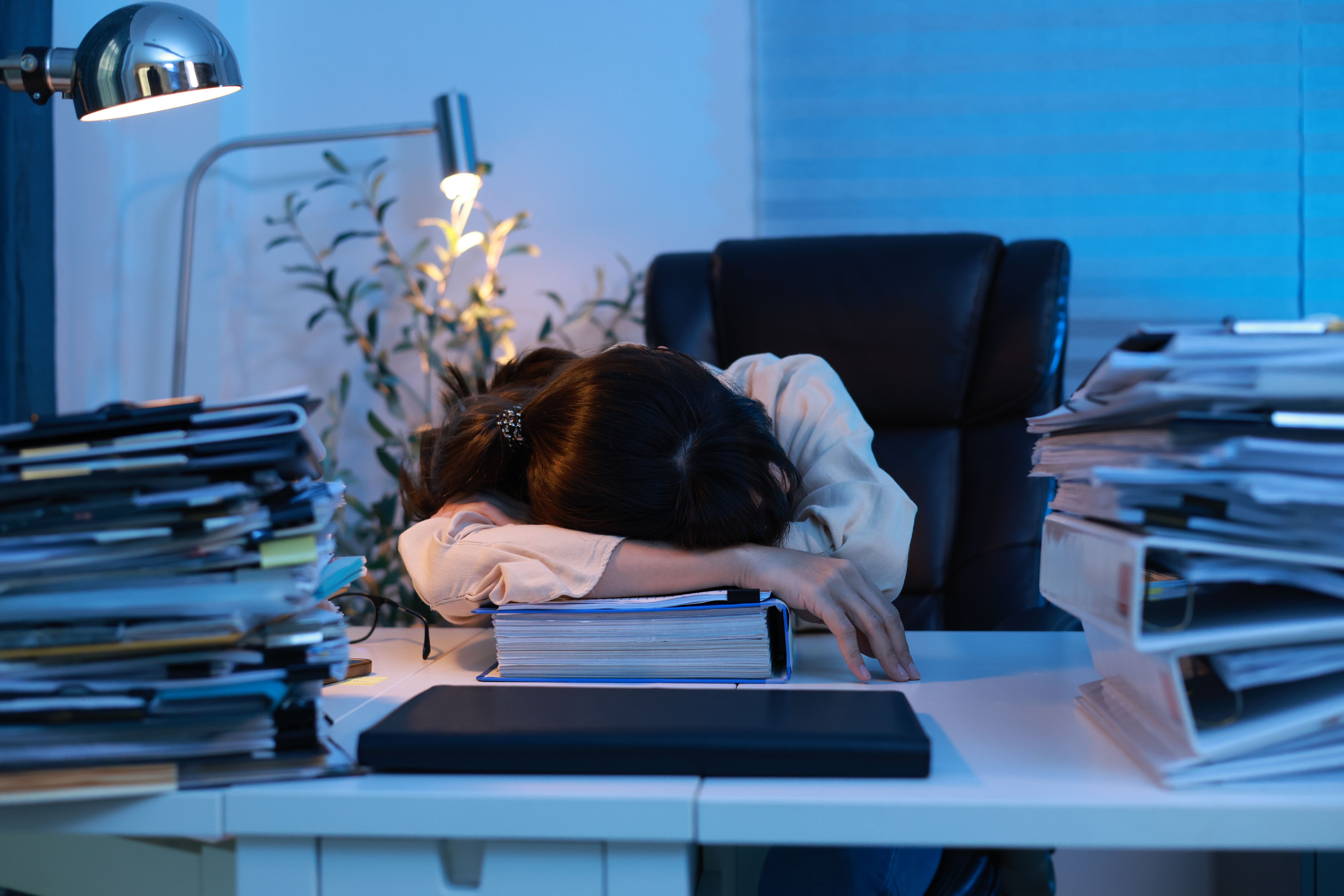 The woman's office was very tired and fell asleep at the workplace, her head lying on the table. A lot of paperwork. Tired employee, a stack of documents and papers. Sleepy tired alone girl dozing off at the table while working hard at late night. The woman's office was very tired and fell asleep at the workplace, her head lying on the table. A lot of paperwork. Tired employee, a stack of documents and papers. Sleepy tired alone girl dozing off at the table while working hard at late night.