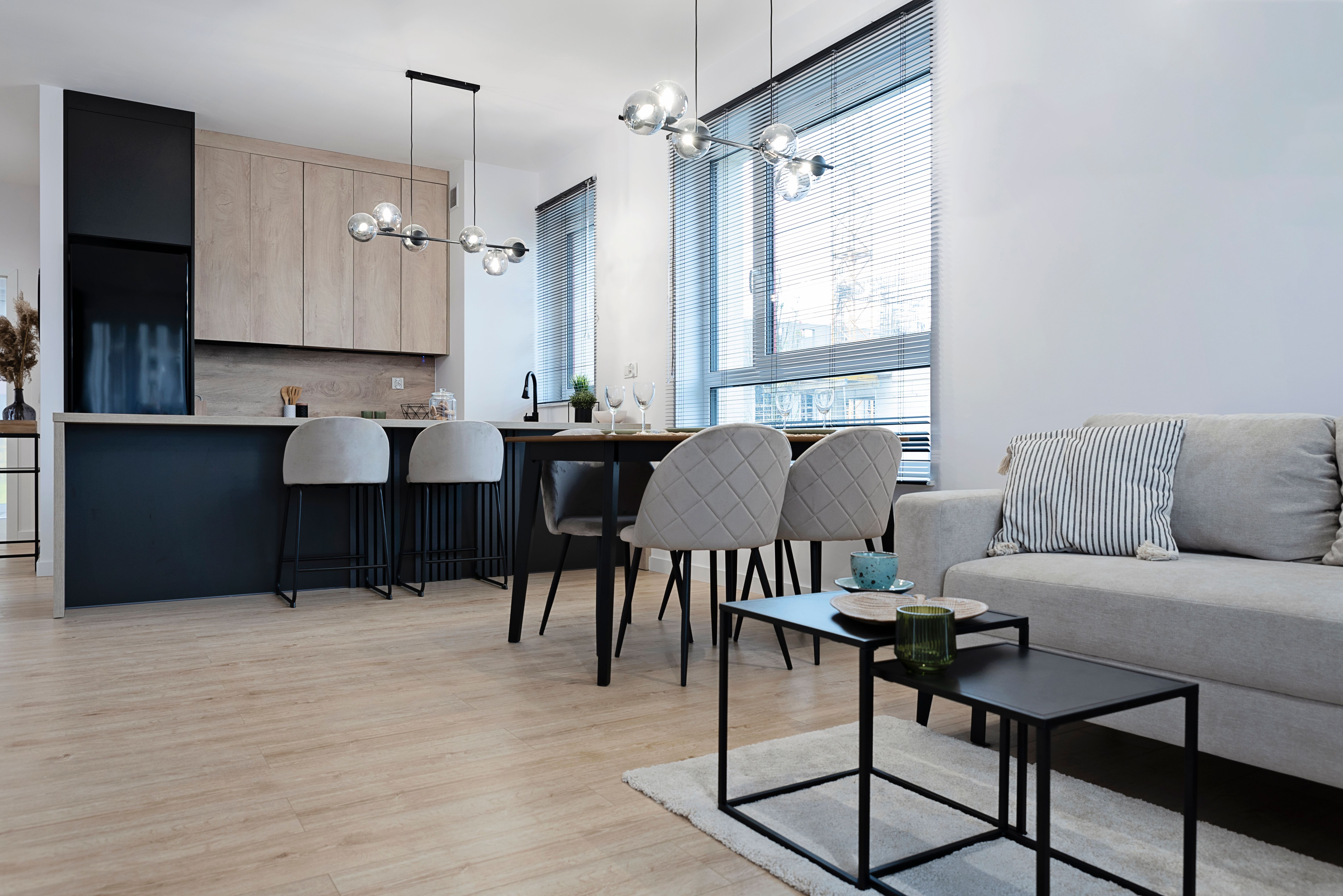Interior decor of living room with kitchen. Comfortable sofa on wooden floor and dining table with chair. Beige color in indoors architecture design. Real estate.
