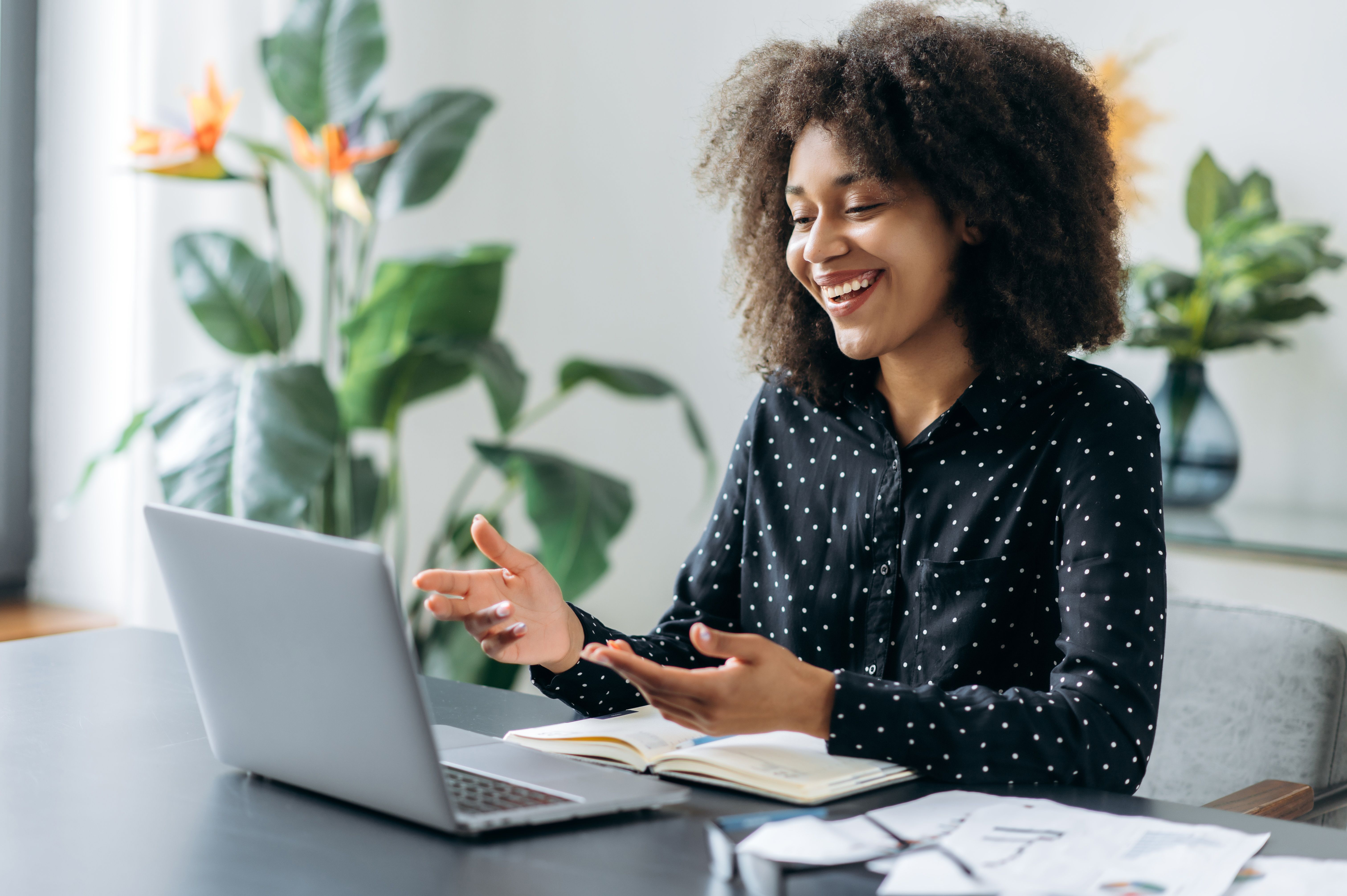 Successful positive young adult woman african woman freelancer, manager, CEO, sitting in office at laptop, talking on video call with client or employees, discussing business strategy, gesturing,smile