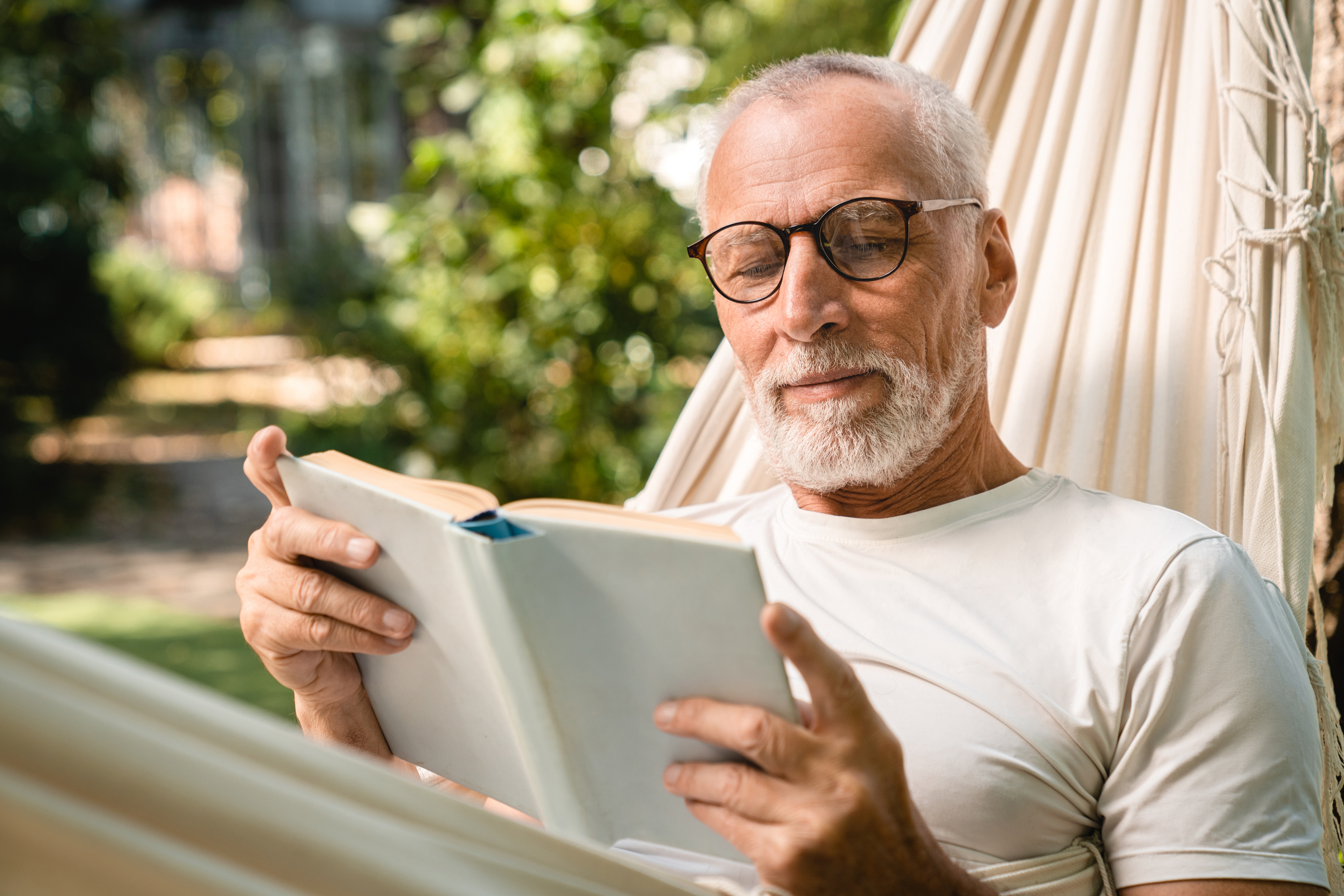 Concentrated grandfather man relaxing resting in hammock while reading book