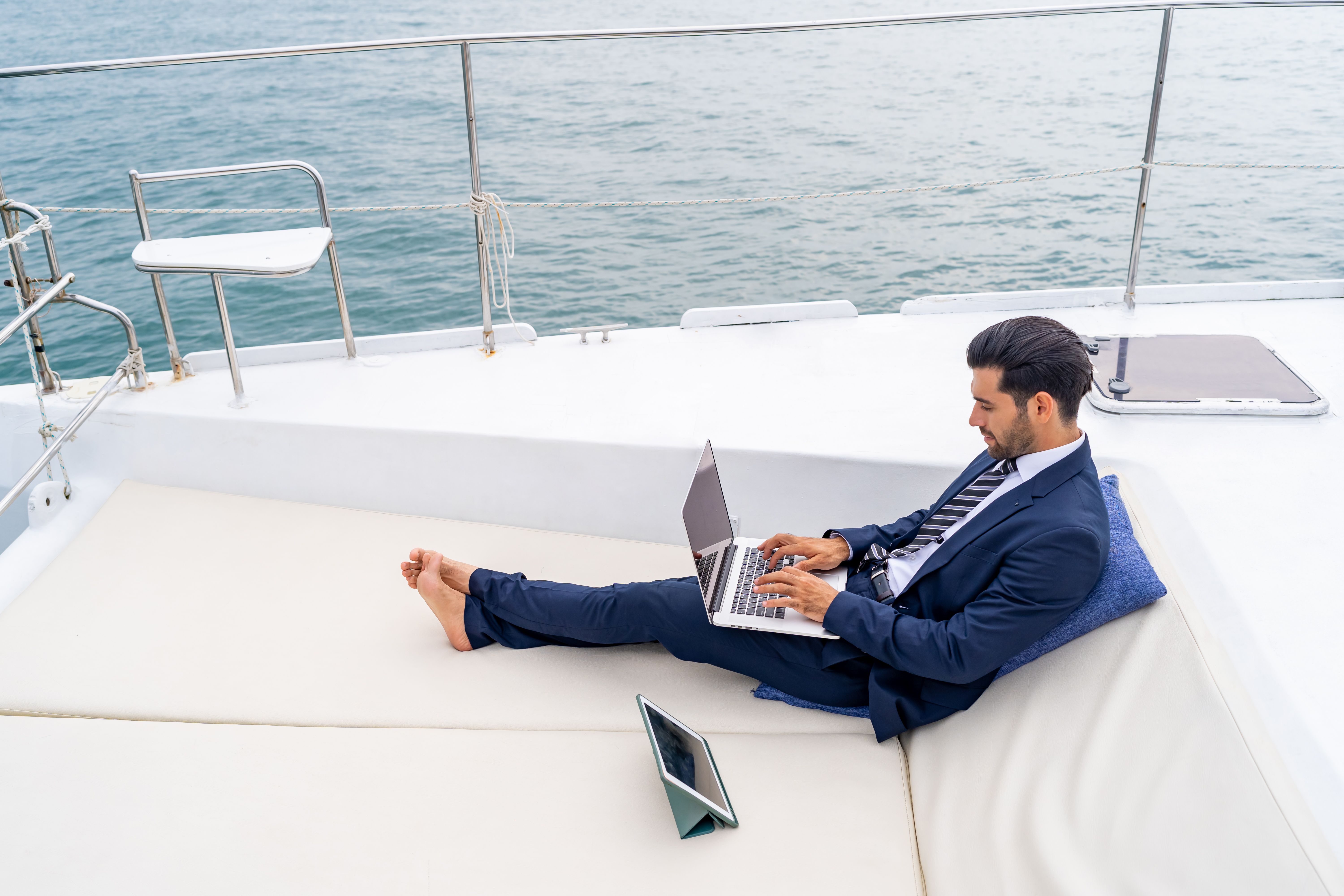Businessman working on laptop with talking on mobile phone while travel on luxury yacht sailing in the ocean