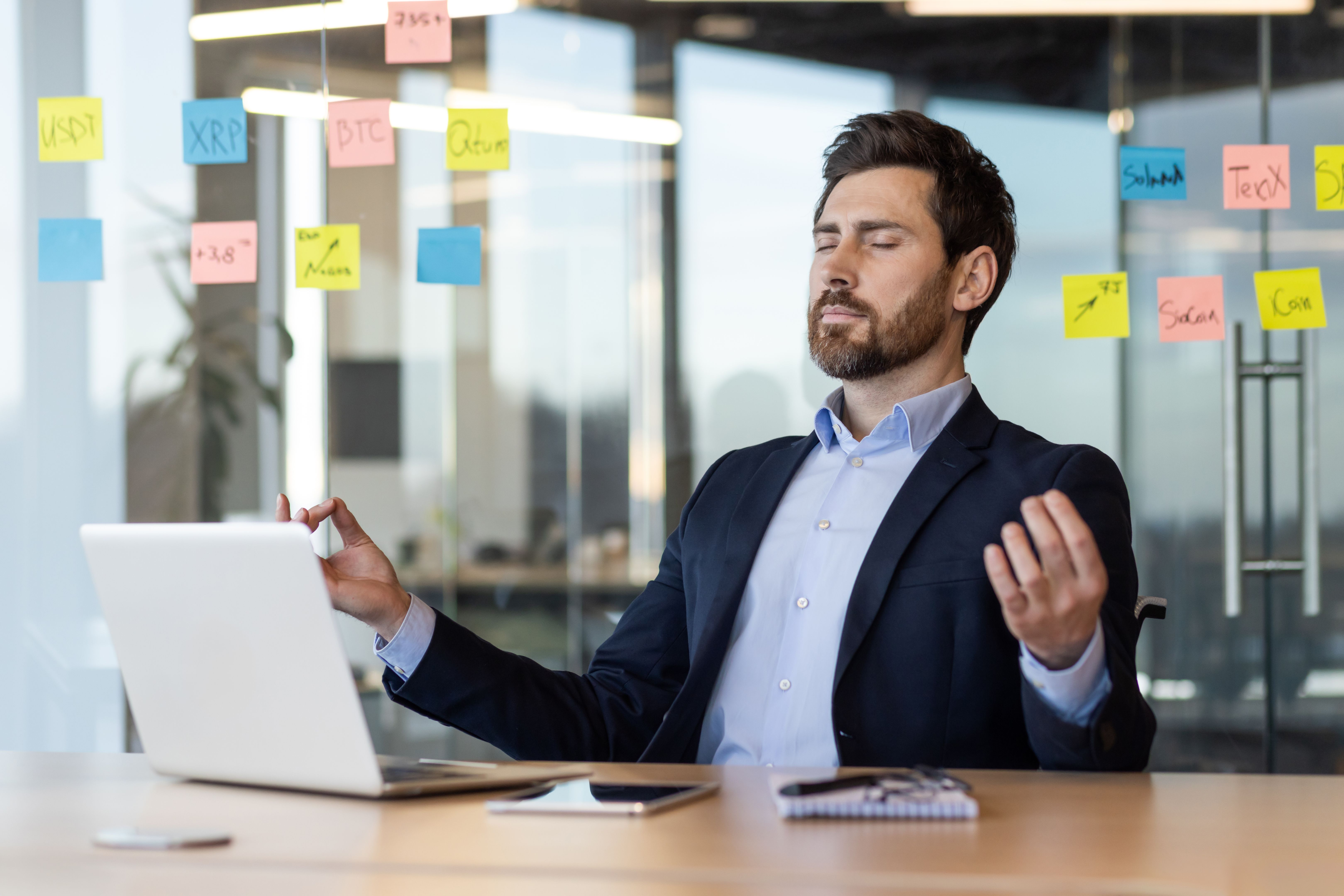 Business professional practicing meditation at office desk surrounded by sticky notes and laptop for stress relief and mindfulness