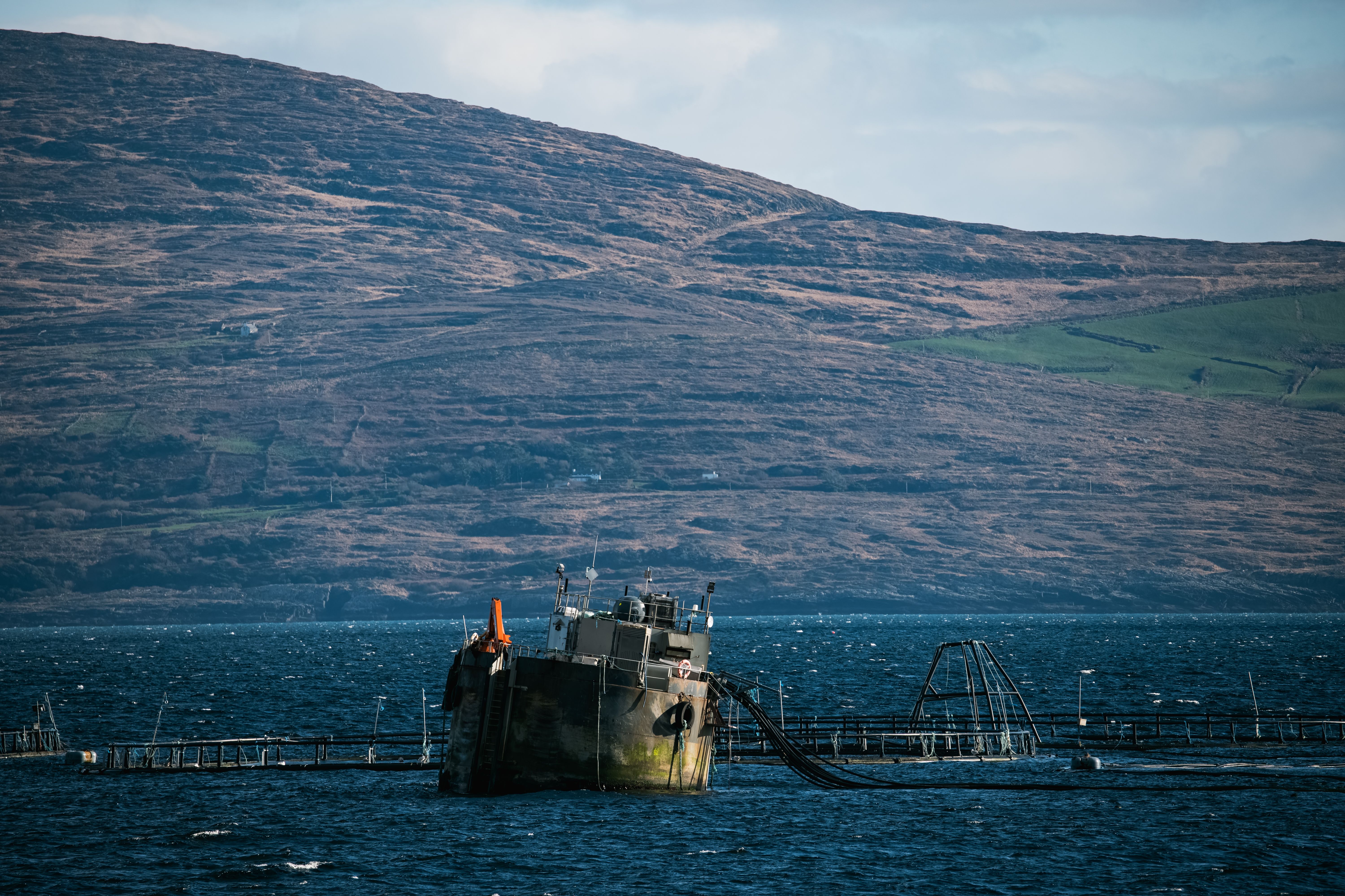 A fish farm, with lush hills rising in the background under a cloudy sky.