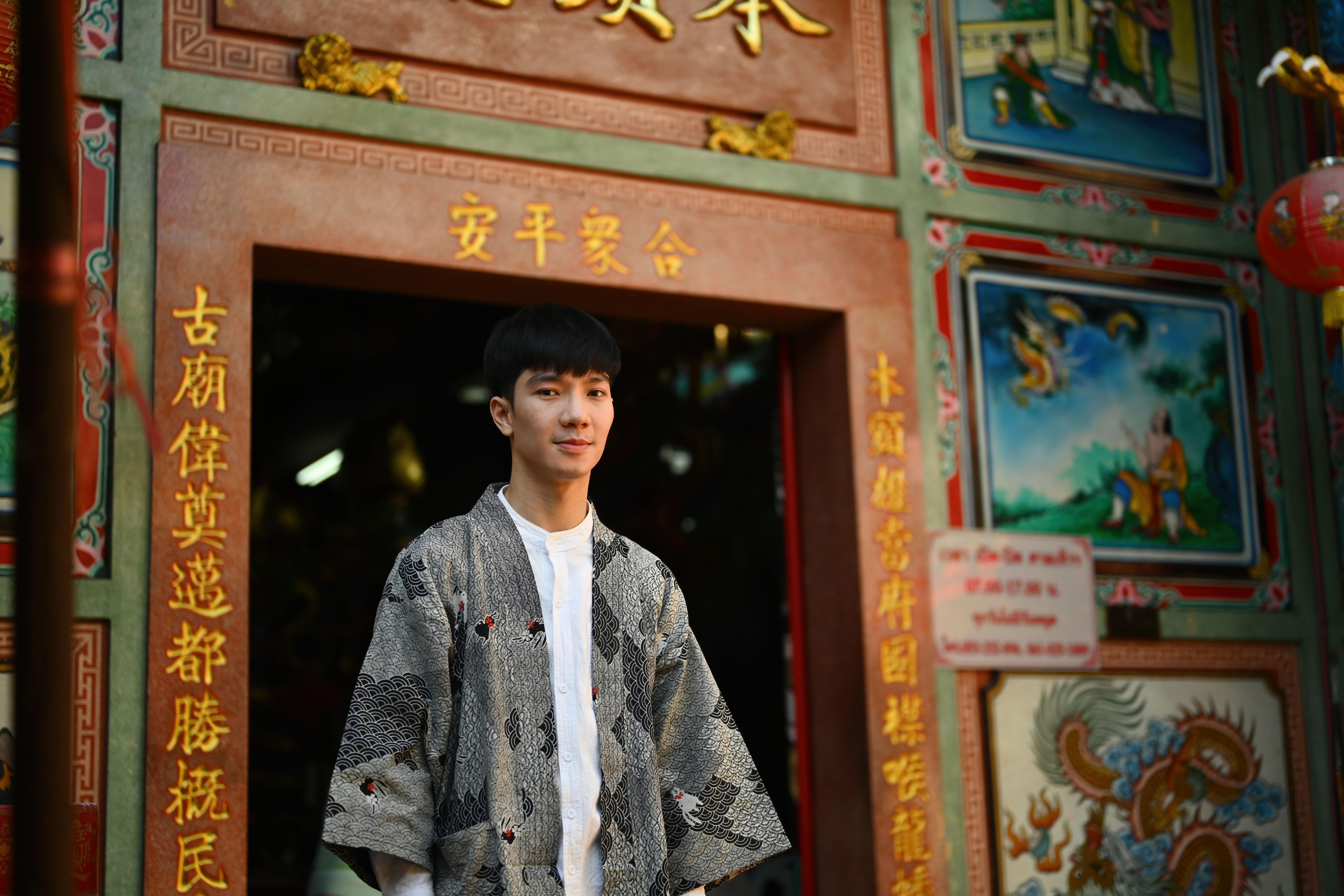 Portrait of a happy and smiling young Asian man wearing a robe standing in front of the entrance to a Chinese shrine