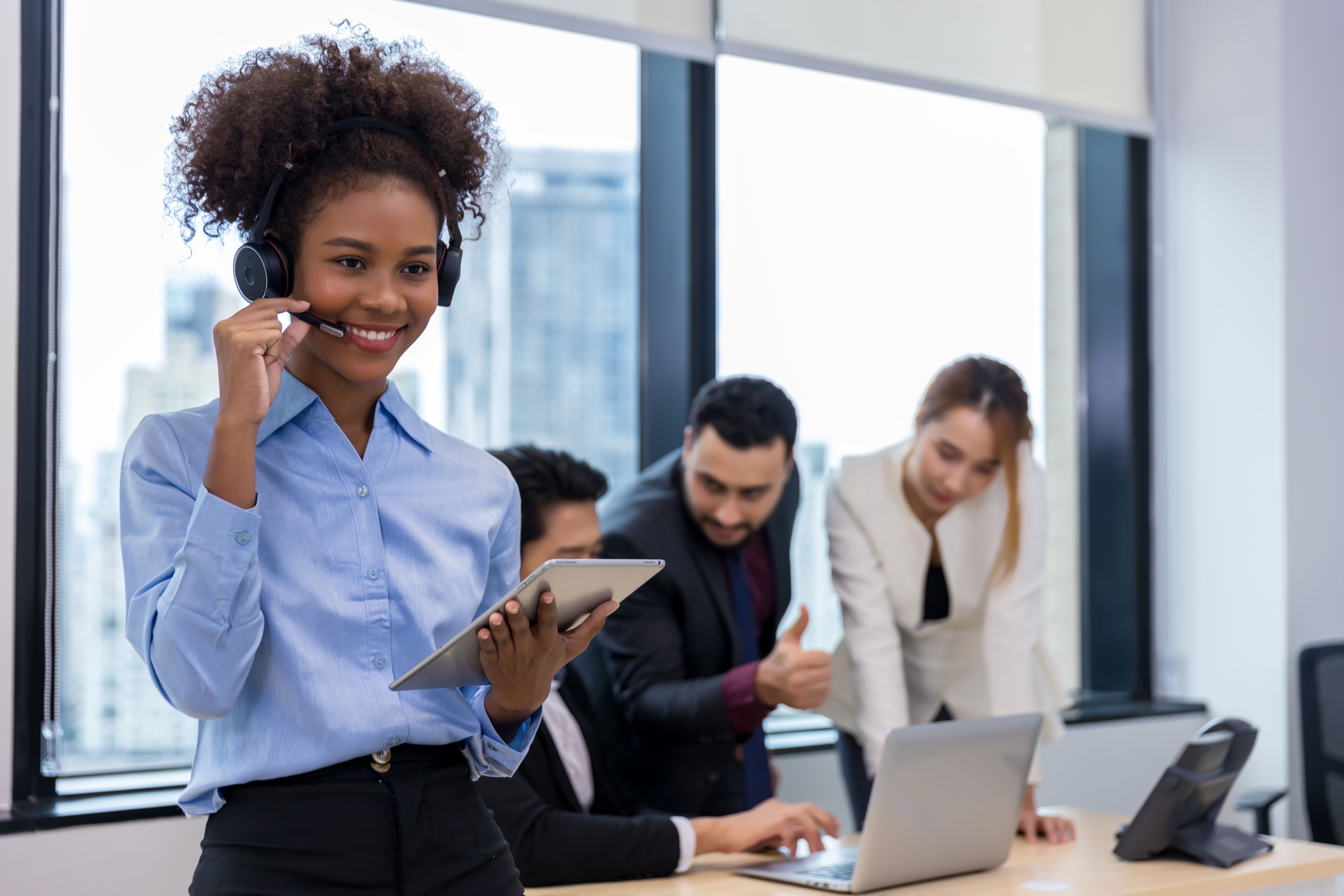 Call center business woman talking on headset. Call center worker accompanied by her team. Customer service executive working at office.