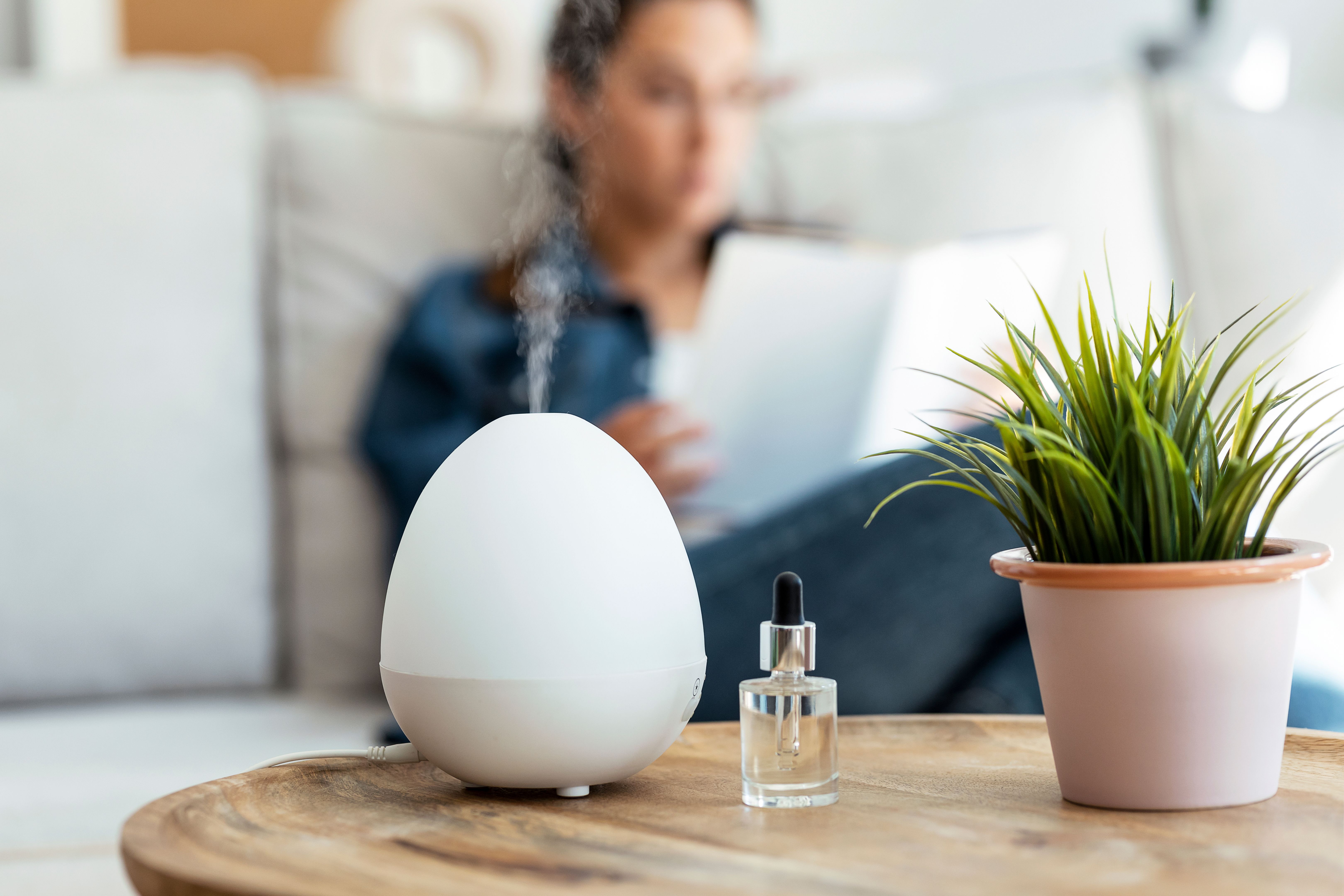 Essential oil aroma diffuser humidifier diffusing water articles in the air while woman reading a book sitting on coach.