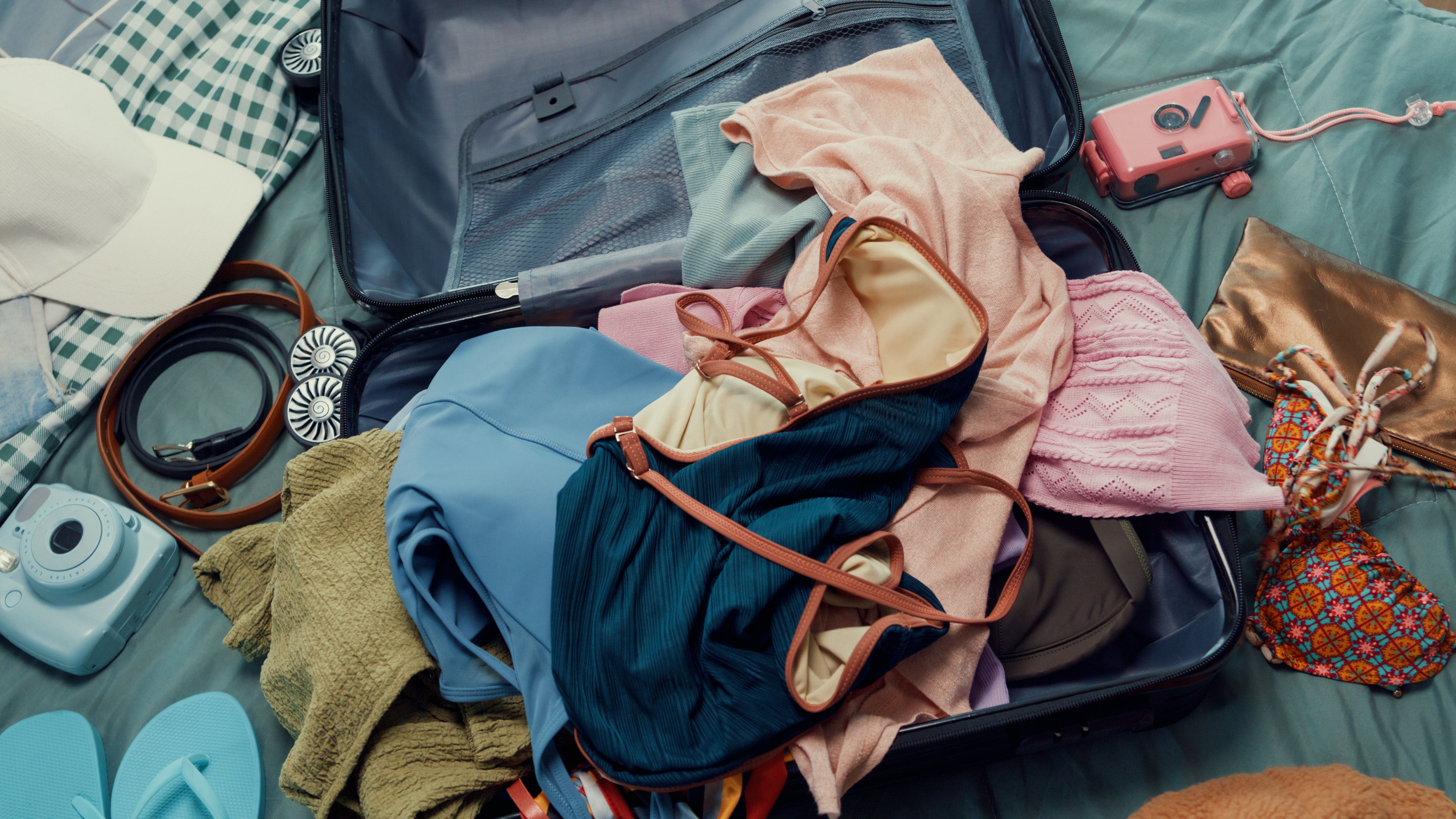 Top view. Young happy and exciting Asian female ready for summer holidays prepare suitcase throw cloth accessories stuff in bag in bedroom. Preparing luggage for summer vacation trip.