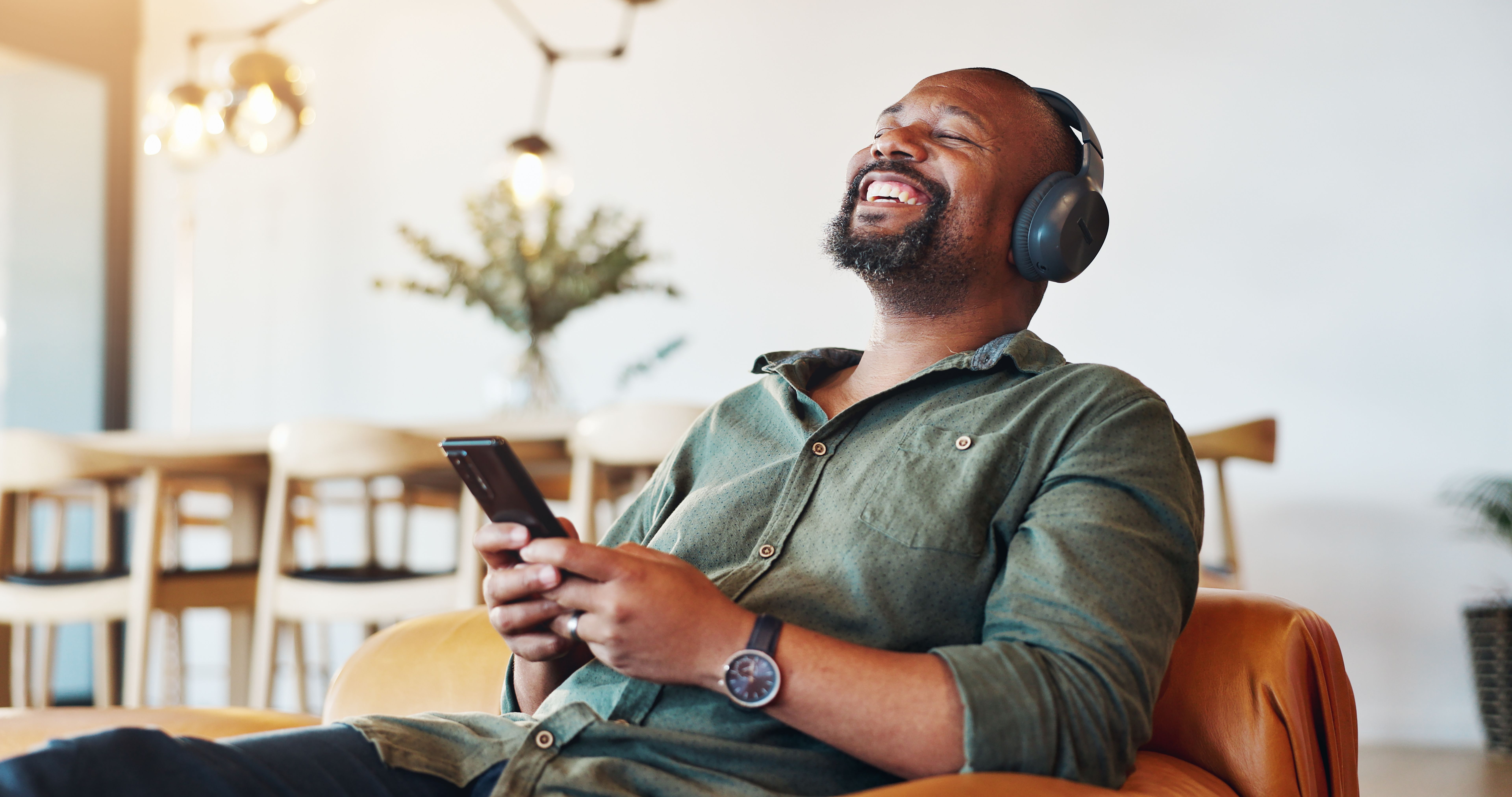 Headphones, phone and black man relax in home with happiness for online music, playlist or album review. Smile, audio tech and African male person with cellphone for streaming radio, podcast or video Headphones, phone and black man relax in home with happiness for online music, playlist or album review. Smile, audio tech and African male person with cellphone for streaming radio, podcast or video