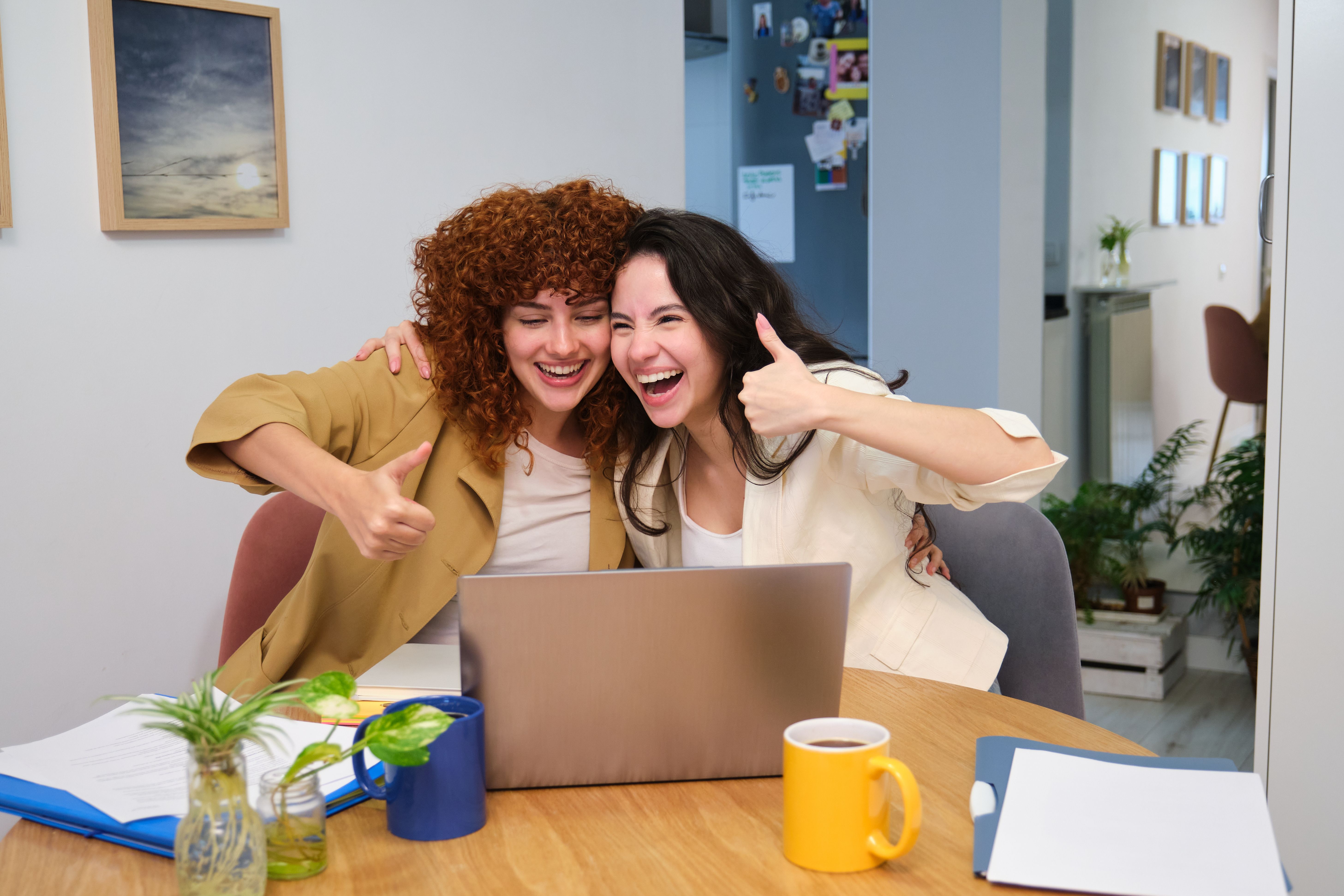 Two happy female entrepreneurs showing thumbs up while working from home