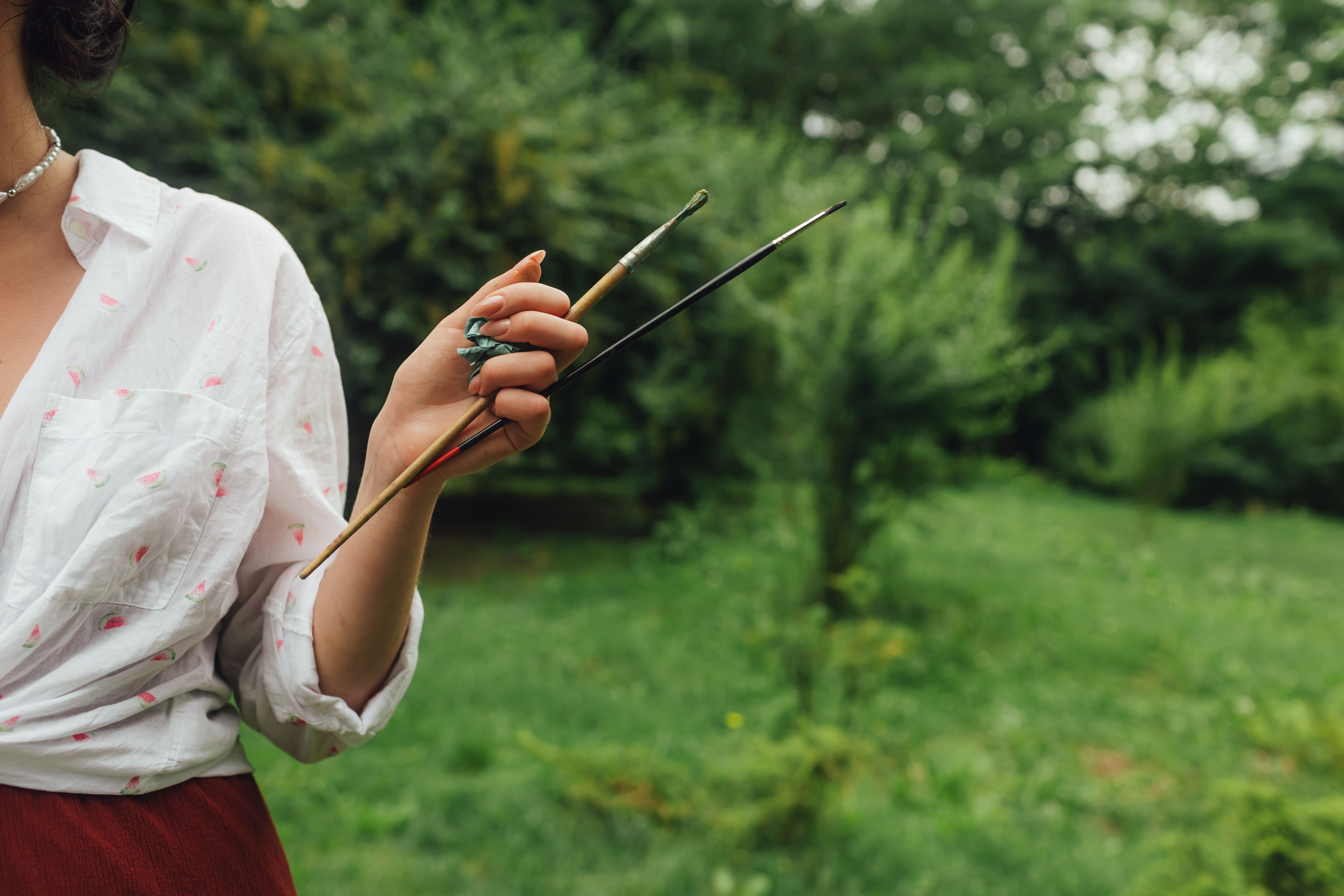 Close up of woman's hands with brushes and paints near a canvas with etude. Mindfulness, art therapy, creativity concept. Process of plein air painting in nature. A series of photos showing the step-by-step creation of a painting