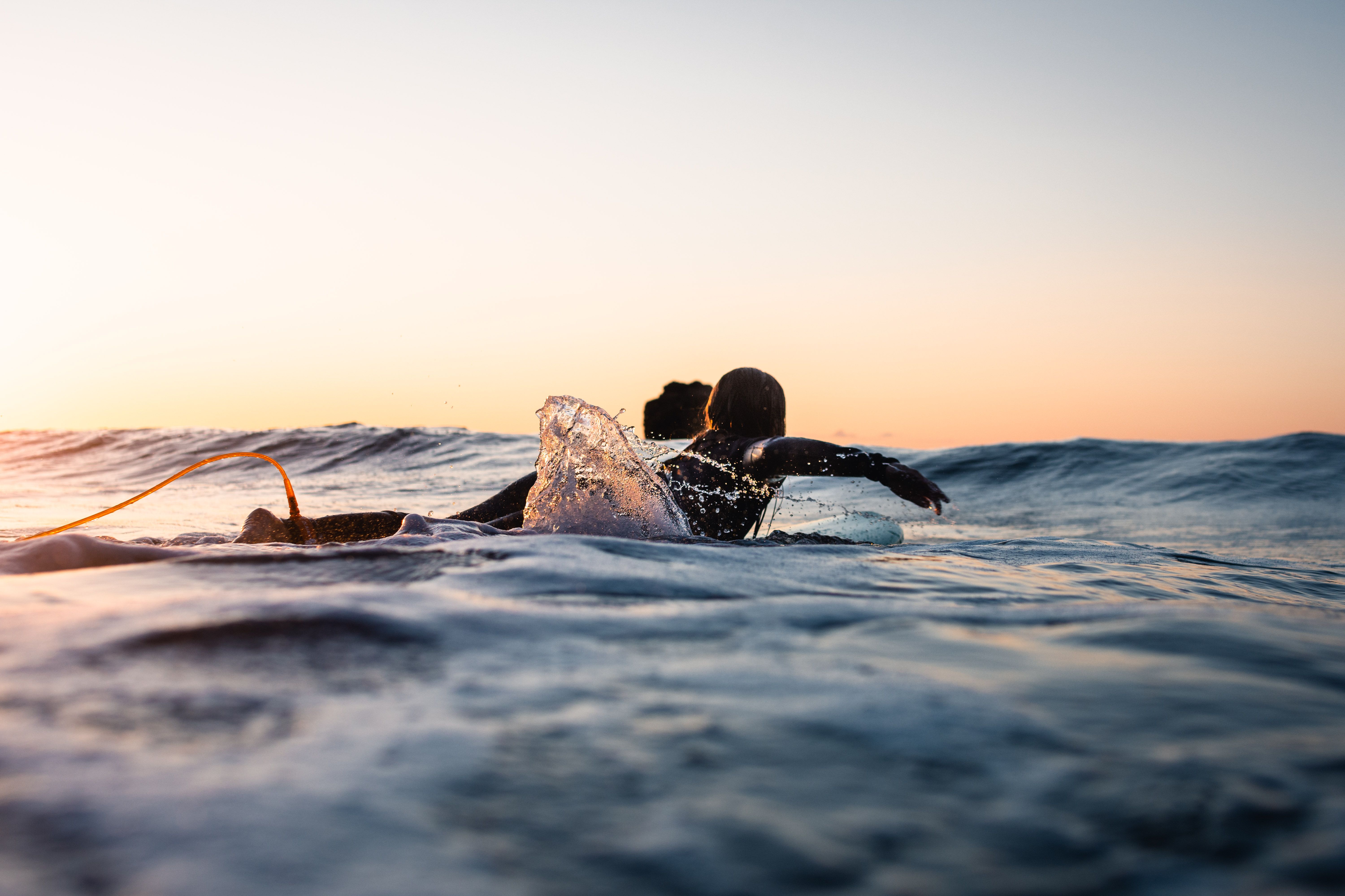 Low angle view of a surfer girl seen from behind. Paddling on a board in the water
