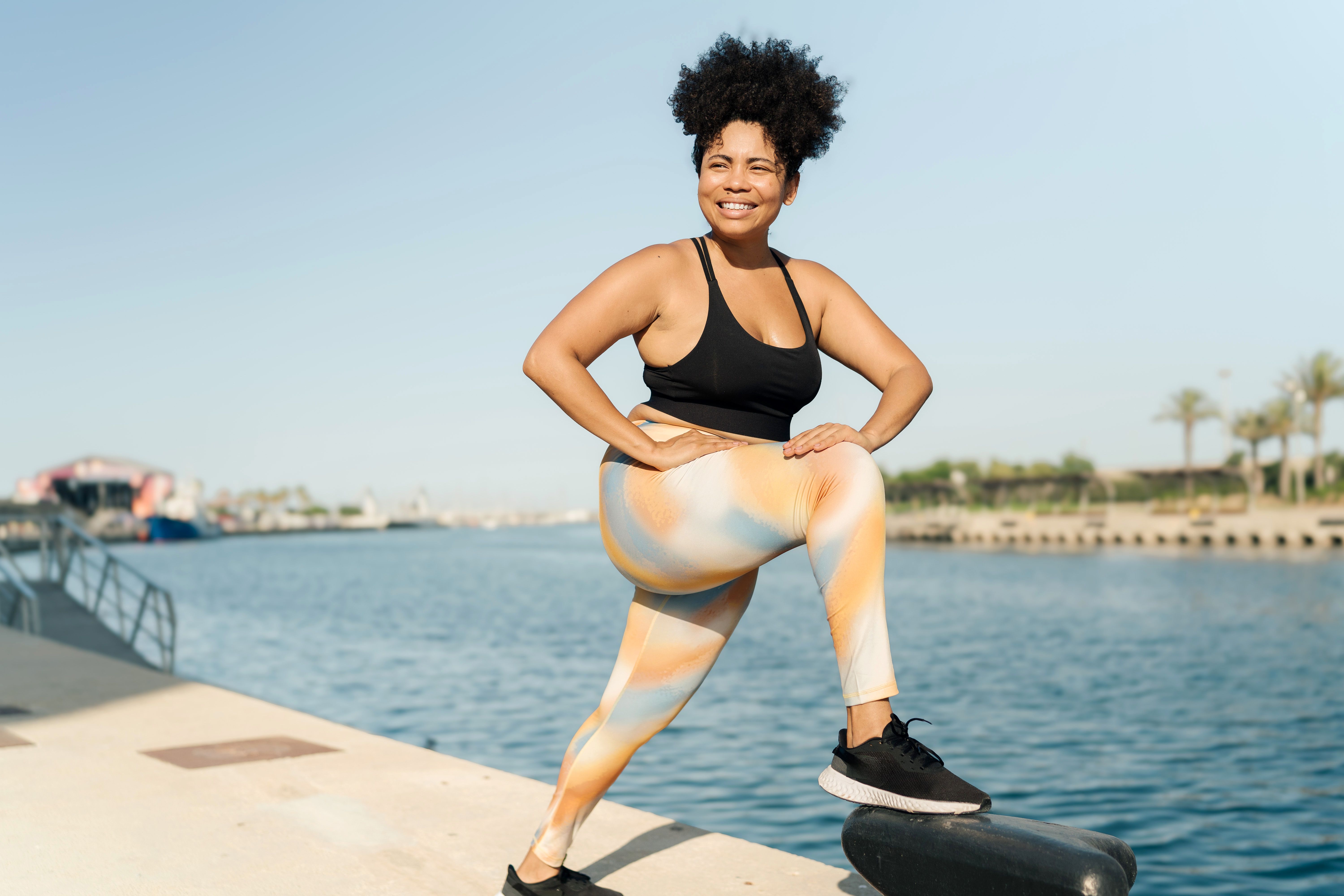 Plus size Hispanic woman in sportswear stretching legs before sport workout at the dock Plus size Hispanic woman in sportswear stretching legs before sport workout at the dock