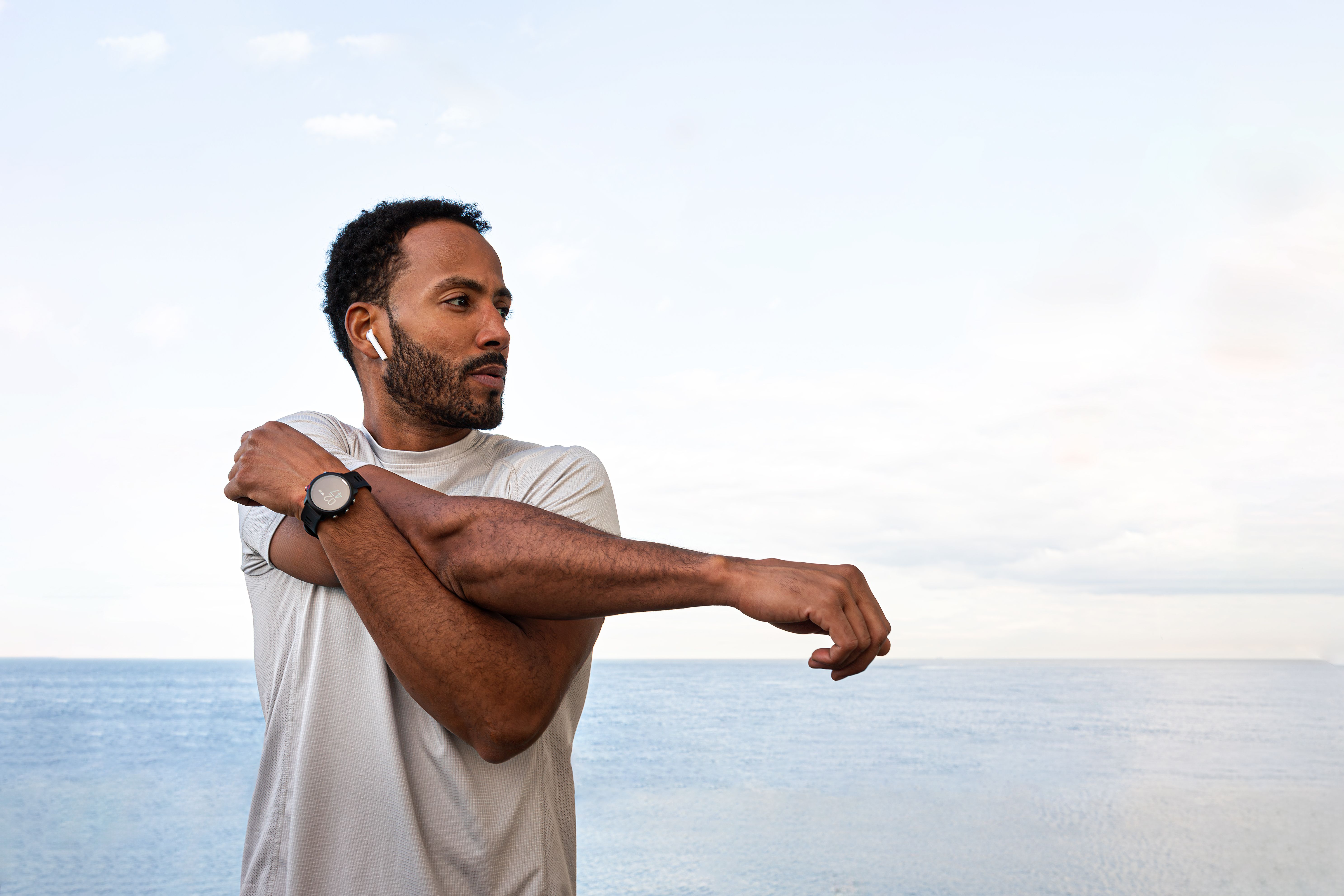 African American man stretching arm, warming up before workout and running session outdoors. Exercising near the ocean.