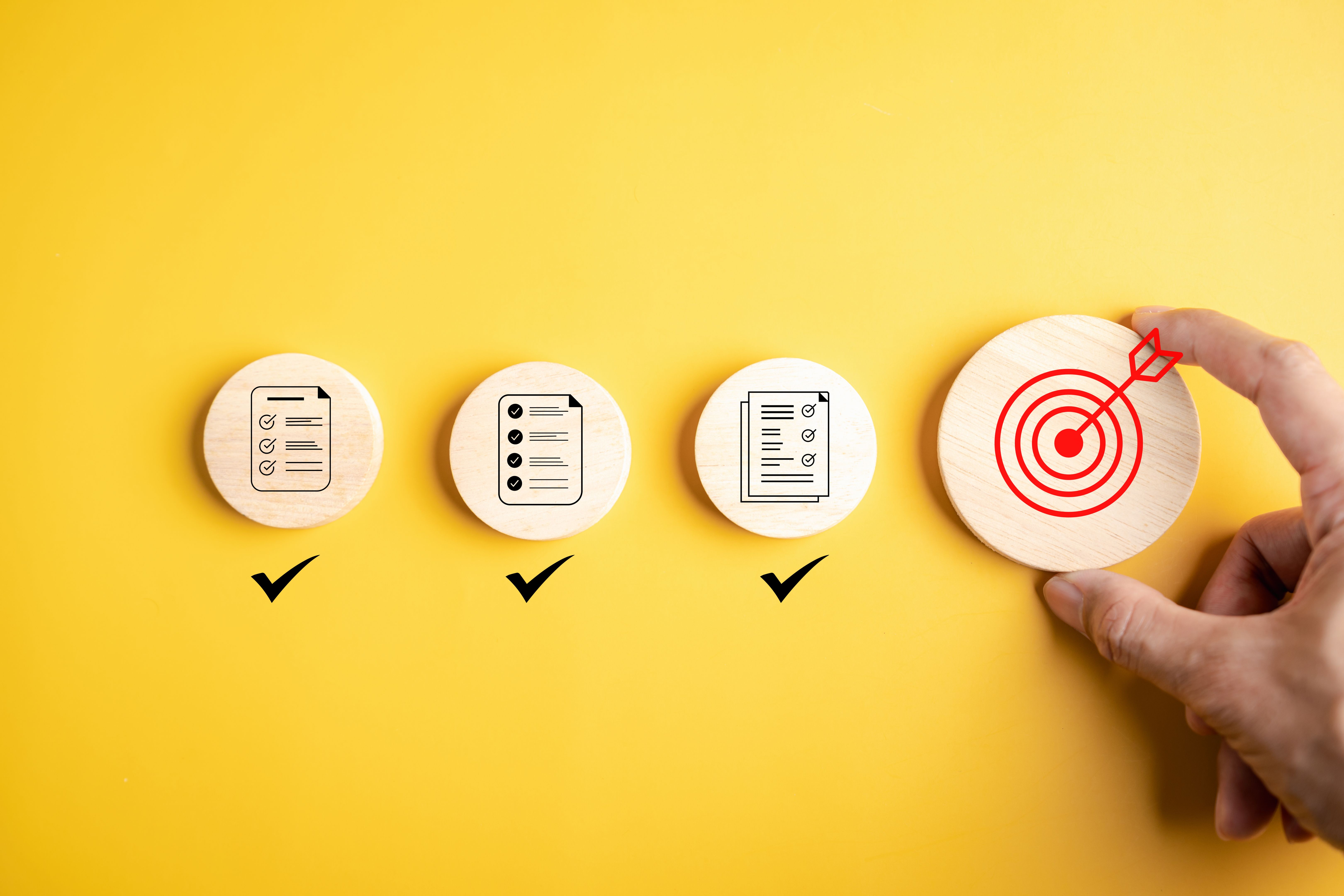 Goal planning and task completion strategy concept. Hand holding target icon after completing all checklist. Wooden blocks on yellow background progress to success. Goal planning and task completion strategy concept. Hand holding target icon after completing all checklist. Wooden blocks on yellow background progress to success.