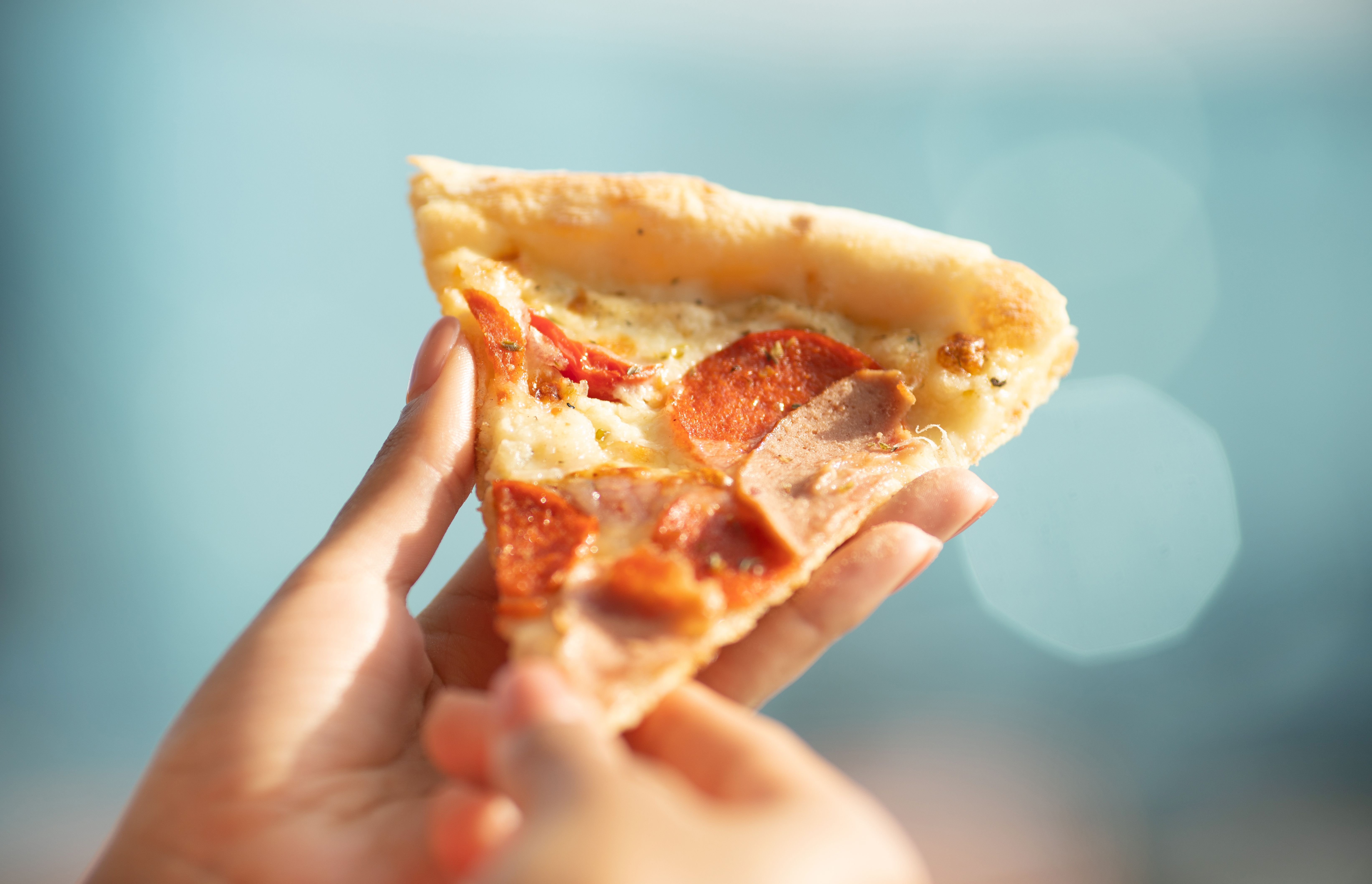 Hot pizza slice with melting cheese. Close up Italian pizza with cheese it stick. Selective focus. Blurred background.