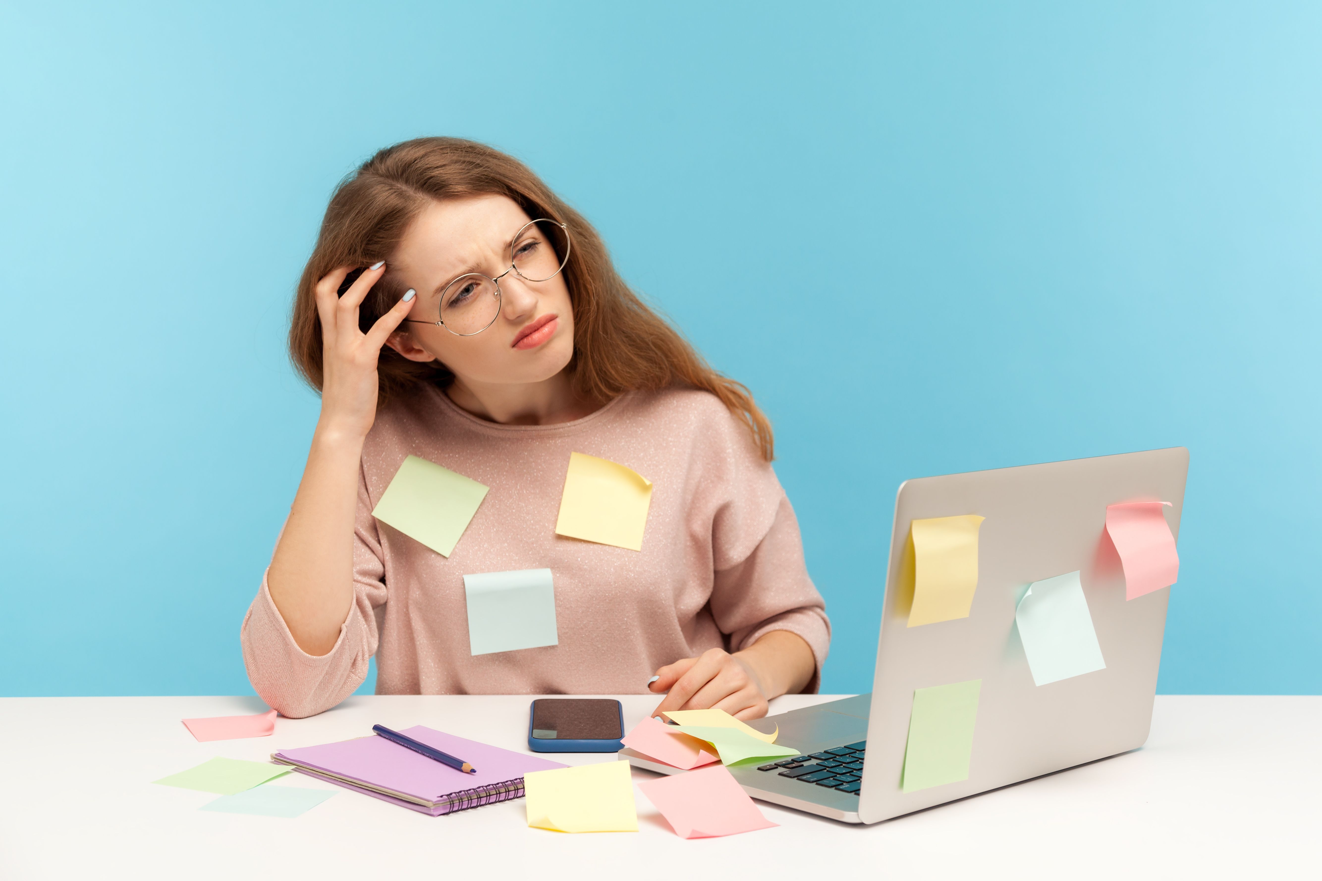 Pensive upset woman employee in nerd eyeglasses sitting at workplace office, all covered with sticky notes Pensive upset woman employee in nerd eyeglasses sitting at workplace office, all covered with sticky notes
