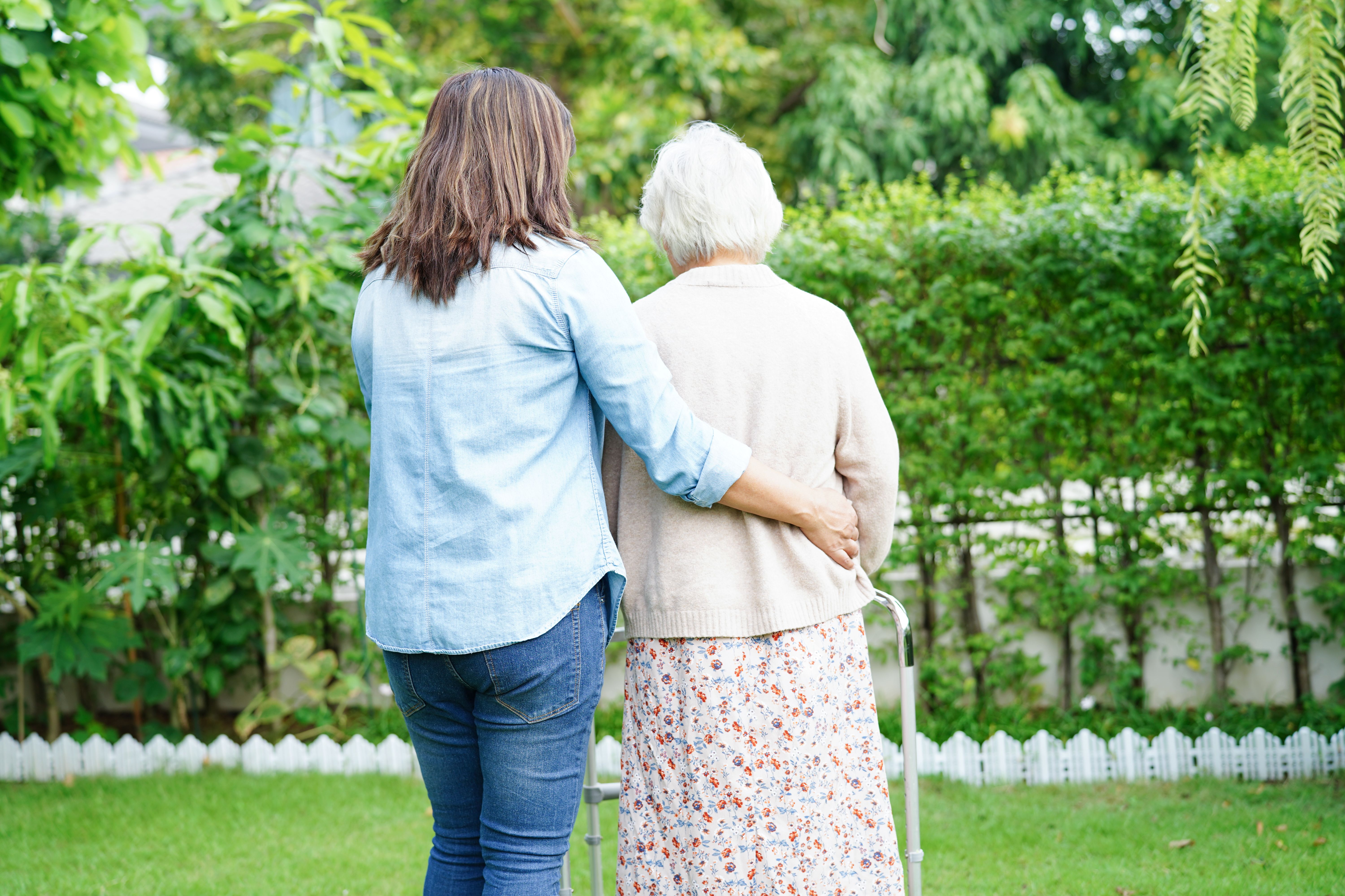 Caregiver help Asian elderly woman disability patient walk with walker in park, medical concept.