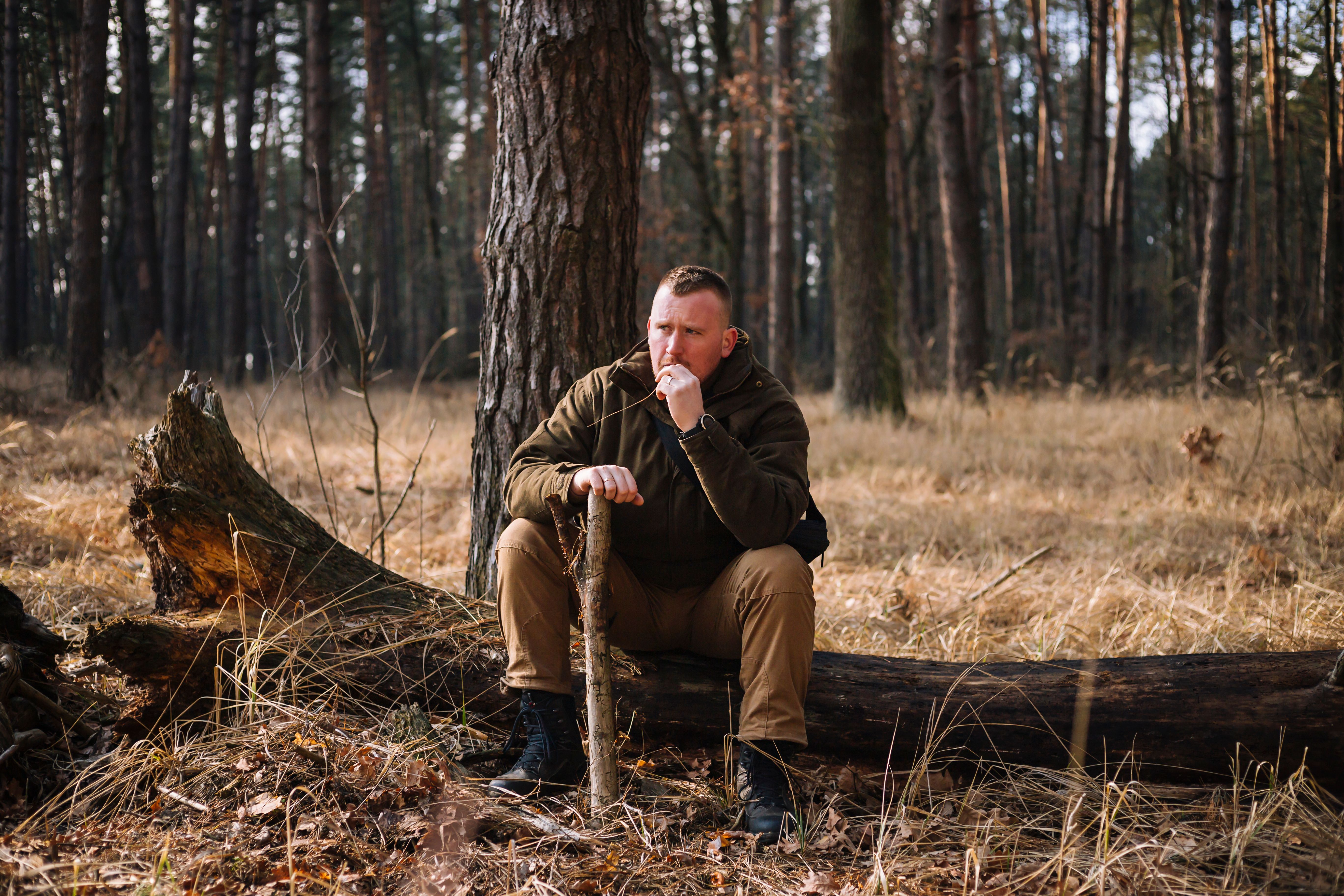 Tough manhood forester sitting on the felled tree trunk in brown clothes